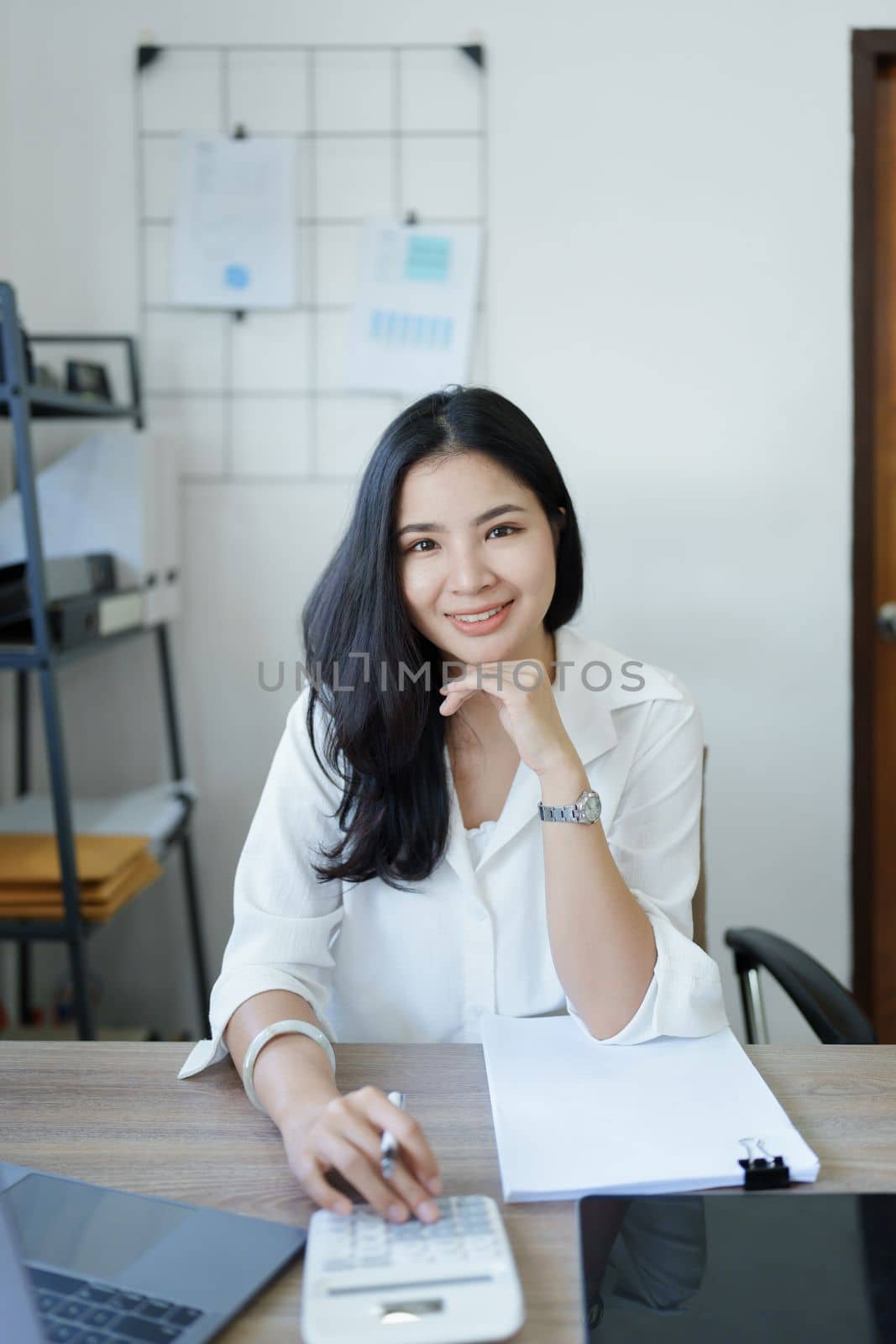 Portrait of a woman business owner showing a happy smiling face as he has successfully invested her business using computers and financial budget documents at work by Manastrong