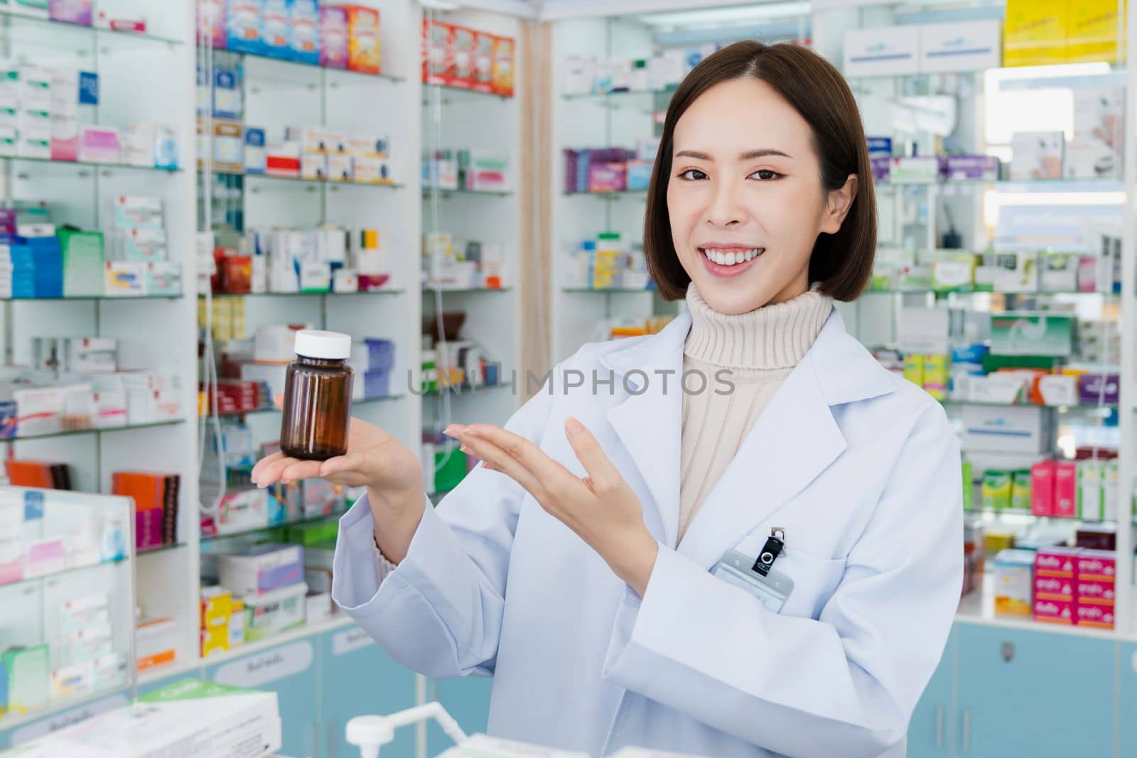 Portrait of young affable pharmacist show qualified medicine pill bottle mockup product for copyspace at pharmacy. Druggist working with her diary job at drugstore, medicine box on shelf at background