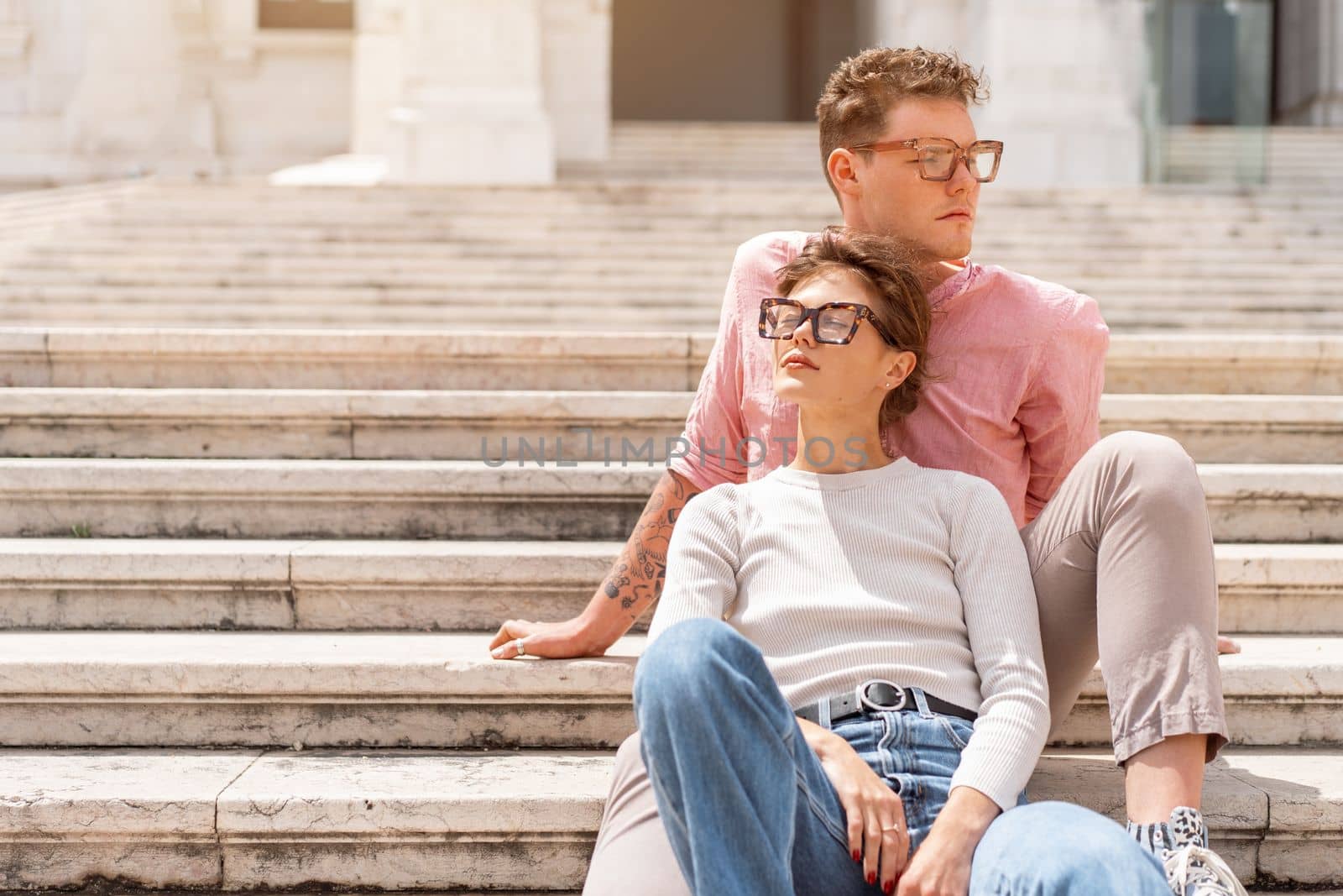 Young beautiful hipster couple in love sitting stairs on old city street, summer Europe vacation, travel, fun, happy, smiling, glasses, trendy outfit, romance, date, embracing