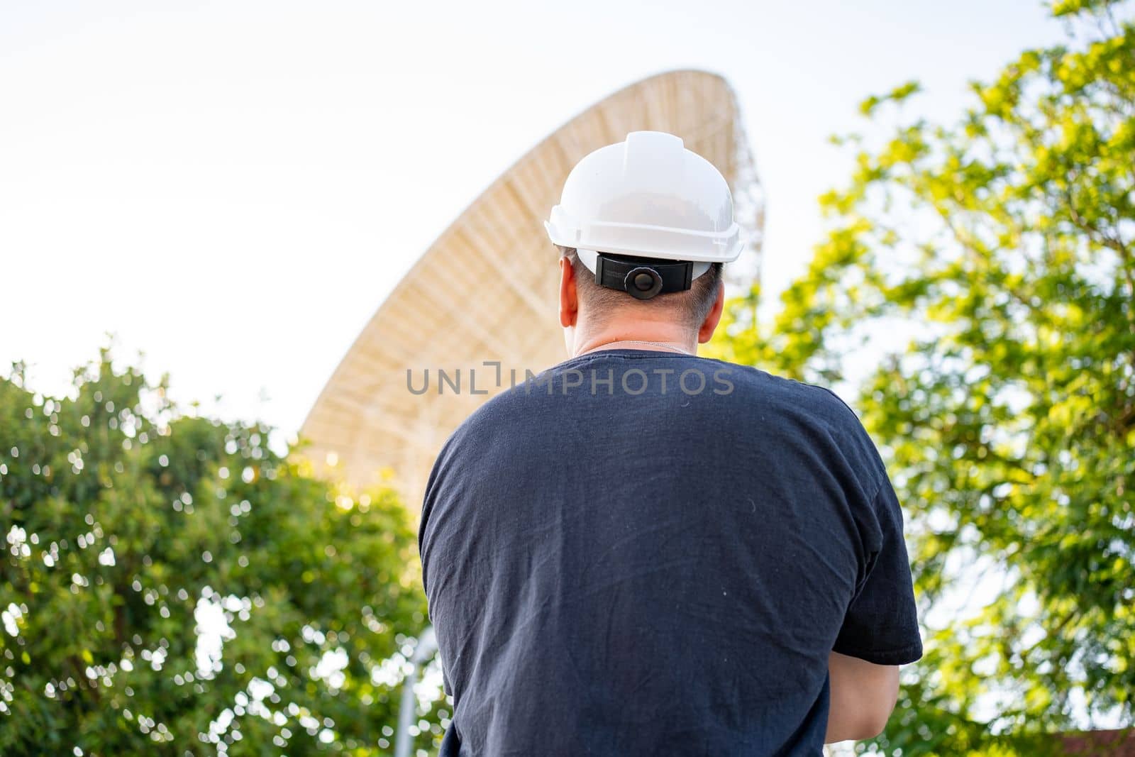 Engineer looking earth based astronomical radio telescope. Radio telescopes used in science for space observation and distant objects exploring. Caucasian man white protective helmet satellite dishes