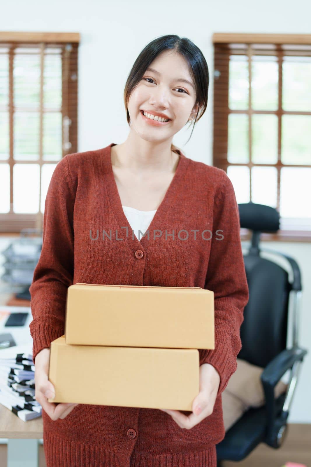 Starting small business entrepreneur of independent Asian woman smiling using computer laptop with cheerful success of online marketing package box items and SME delivery concept.