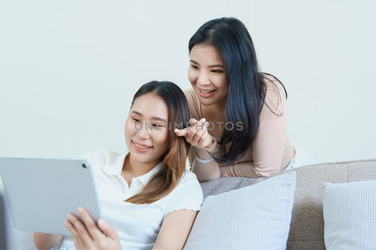 lgbtq, lgbt concept, homosexuality, portrait of two asian women posing happy together and loving each other while playing tablet at sofa by Manastrong