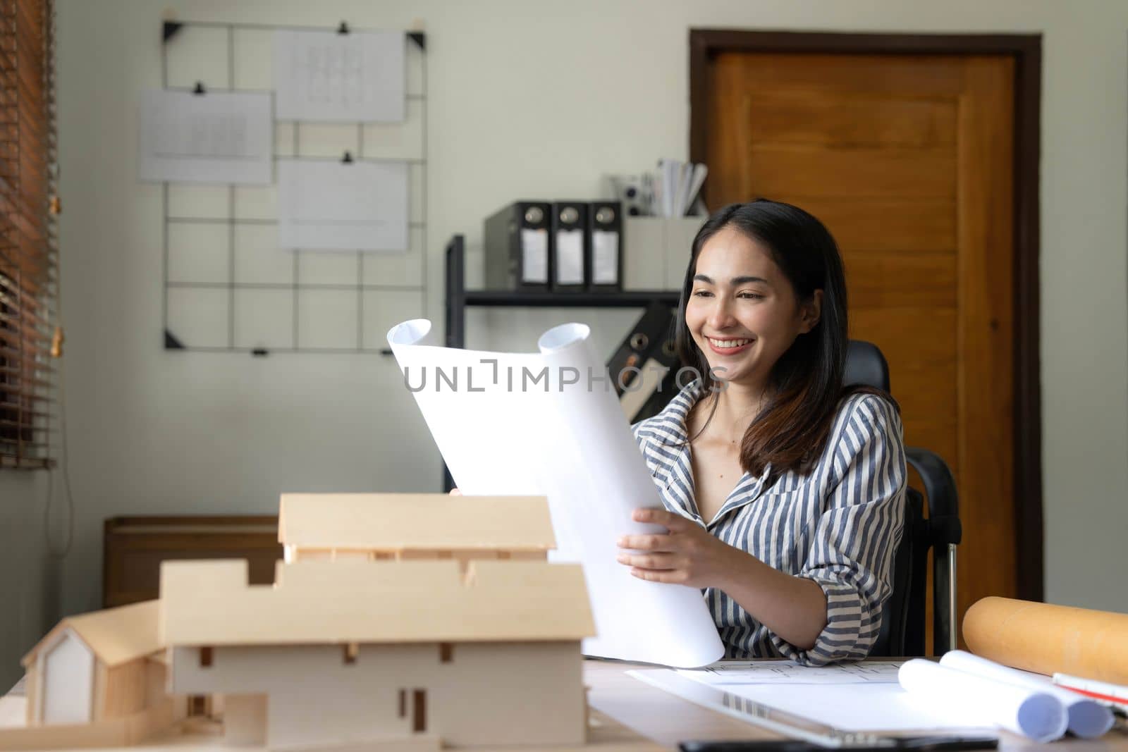 Architecture, building, construction and real estate concept - Happy smiling female architect with blueprint, ruler and living house model on table working at home office. Architect woman