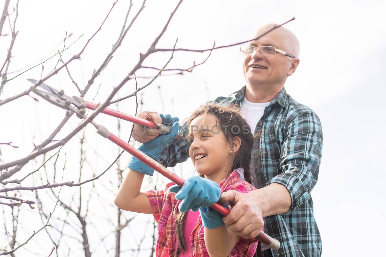 A small girl with grandfather outside in spring nature, having fun. gardening by Andelov13