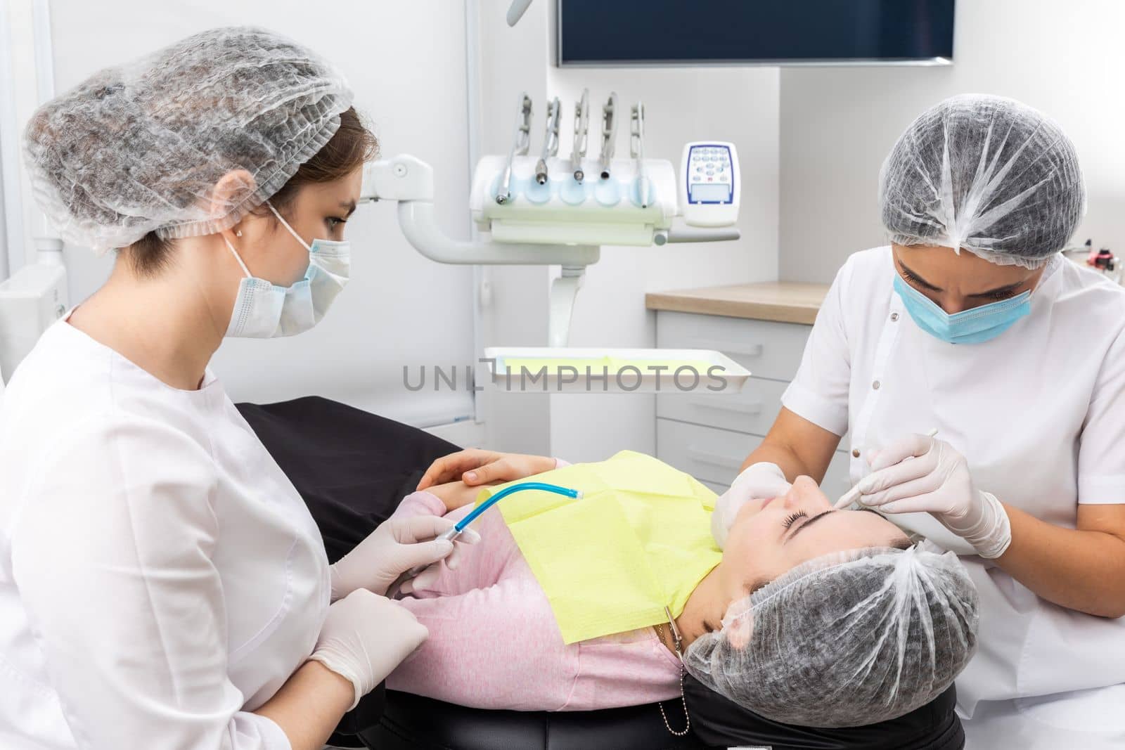 Dentist and assistant performing dental treatment inmodern dental clinic, patient laying in a chair by Mariakray