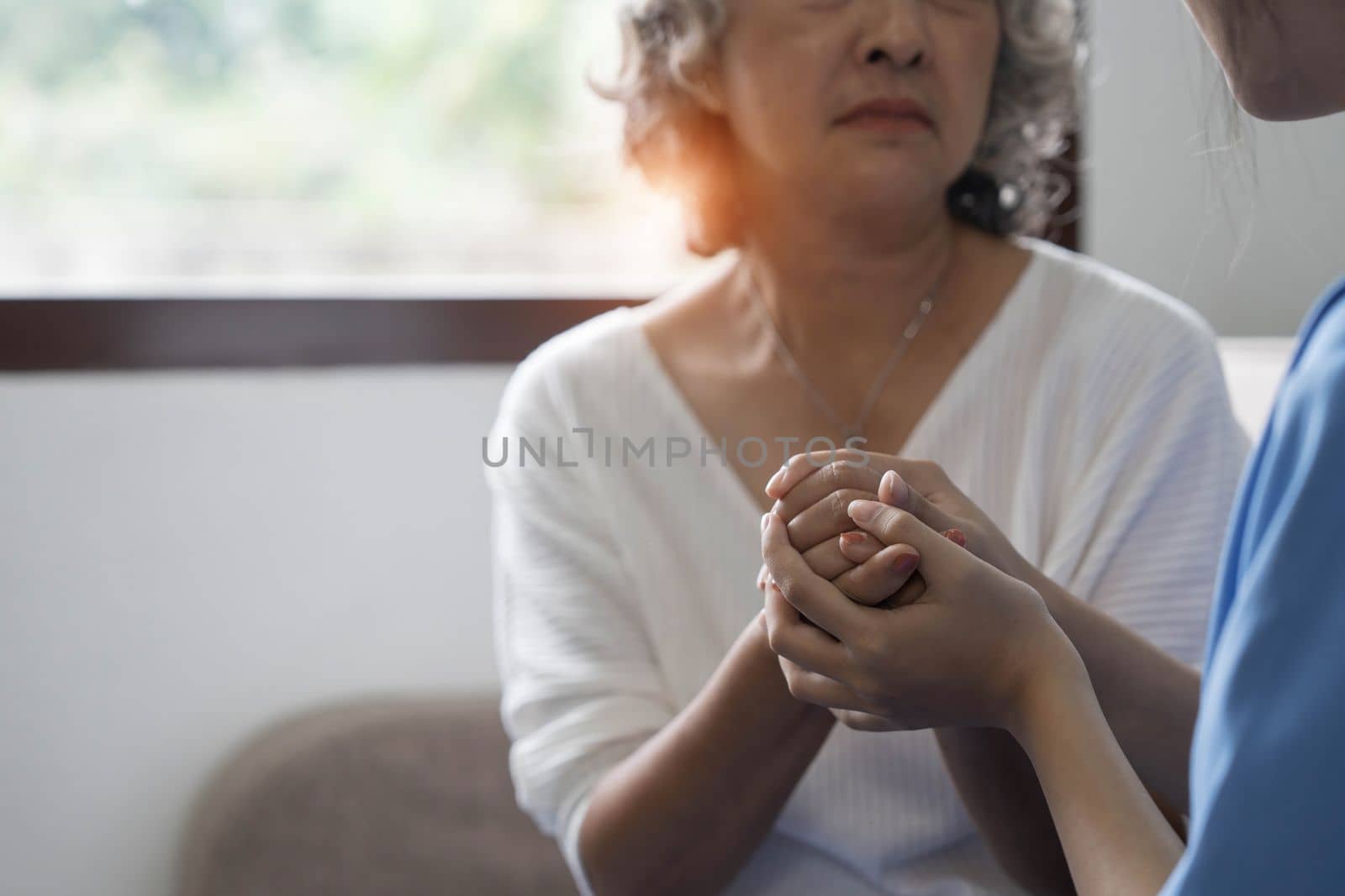 Happy patient is holding caregiver for a hand while spending time together. Elderly woman in nursing home and nurse...