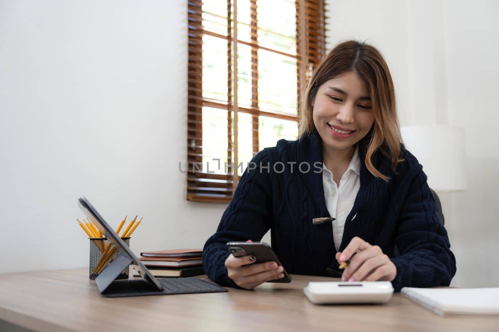 Business asian woman using smartphone for do math finance on wooden desk in office, tax, accounting, financial concept.