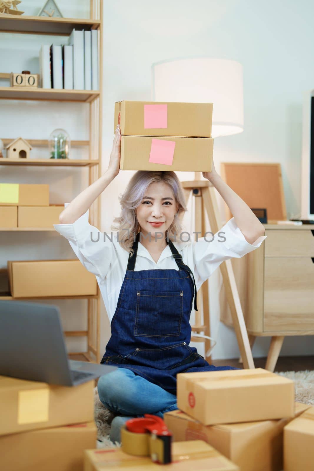 Starting small business entrepreneur of independent Asian woman smiling using computer laptop with cheerful success of online marketing package box items and SME delivery concept.