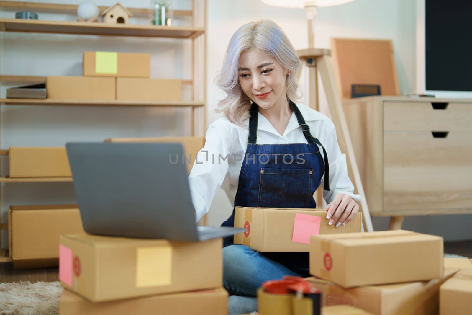 Starting small business entrepreneur of independent Asian woman smiling using computer laptop with cheerful success of online marketing package box items and SME delivery concept by Manastrong