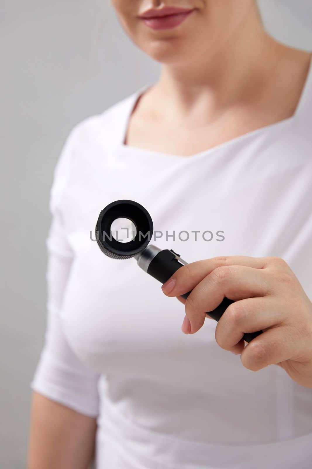 Woman gets professional skin exam at doctor's office. Dermatologist or cosmetology specialist uses magnifying glass to investigate mole, sun damage or potential cancerous tumor on young female face by Mariakray