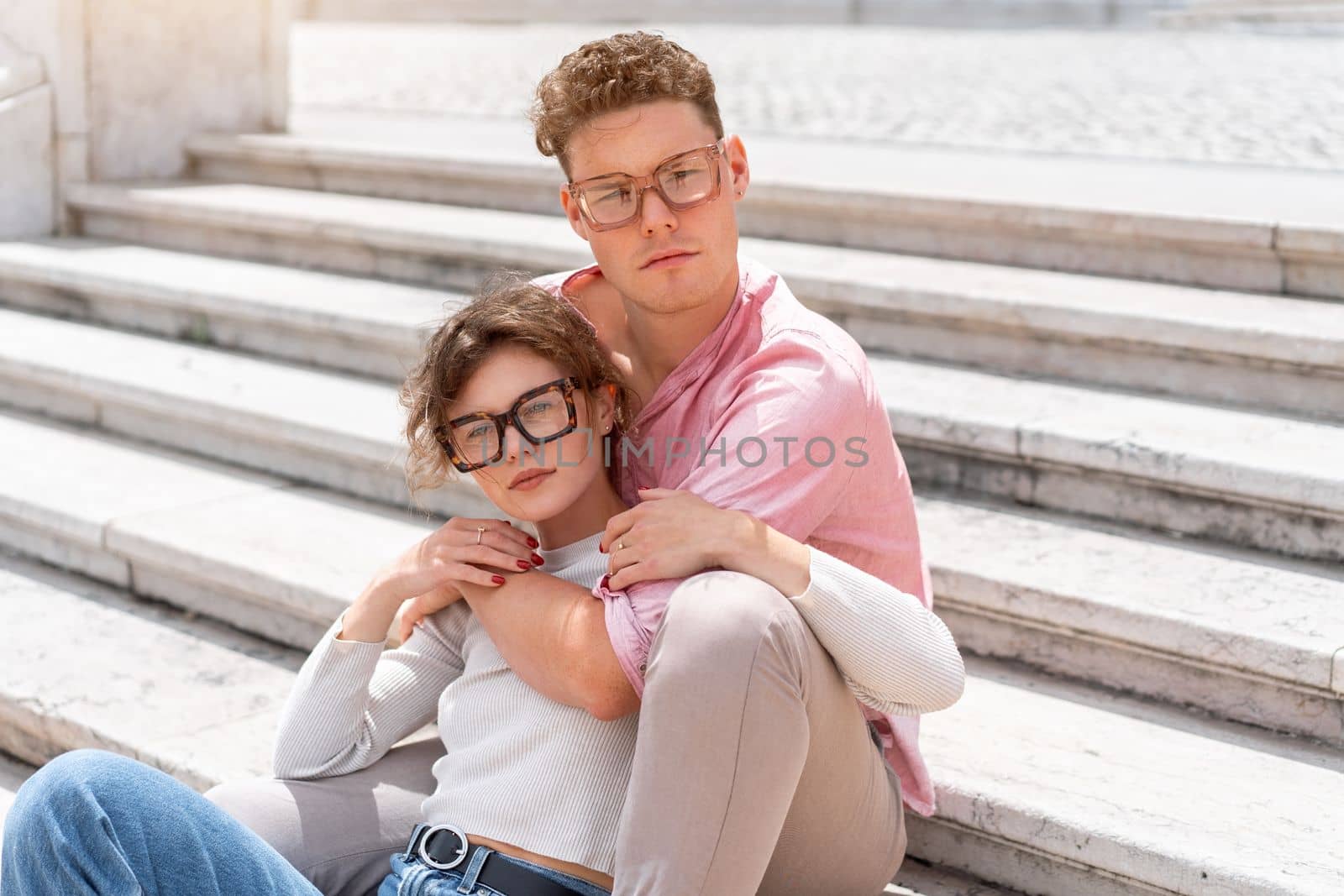 Young beautiful hipster couple in sunglasses in love sitting stairs on old city street by andreonegin