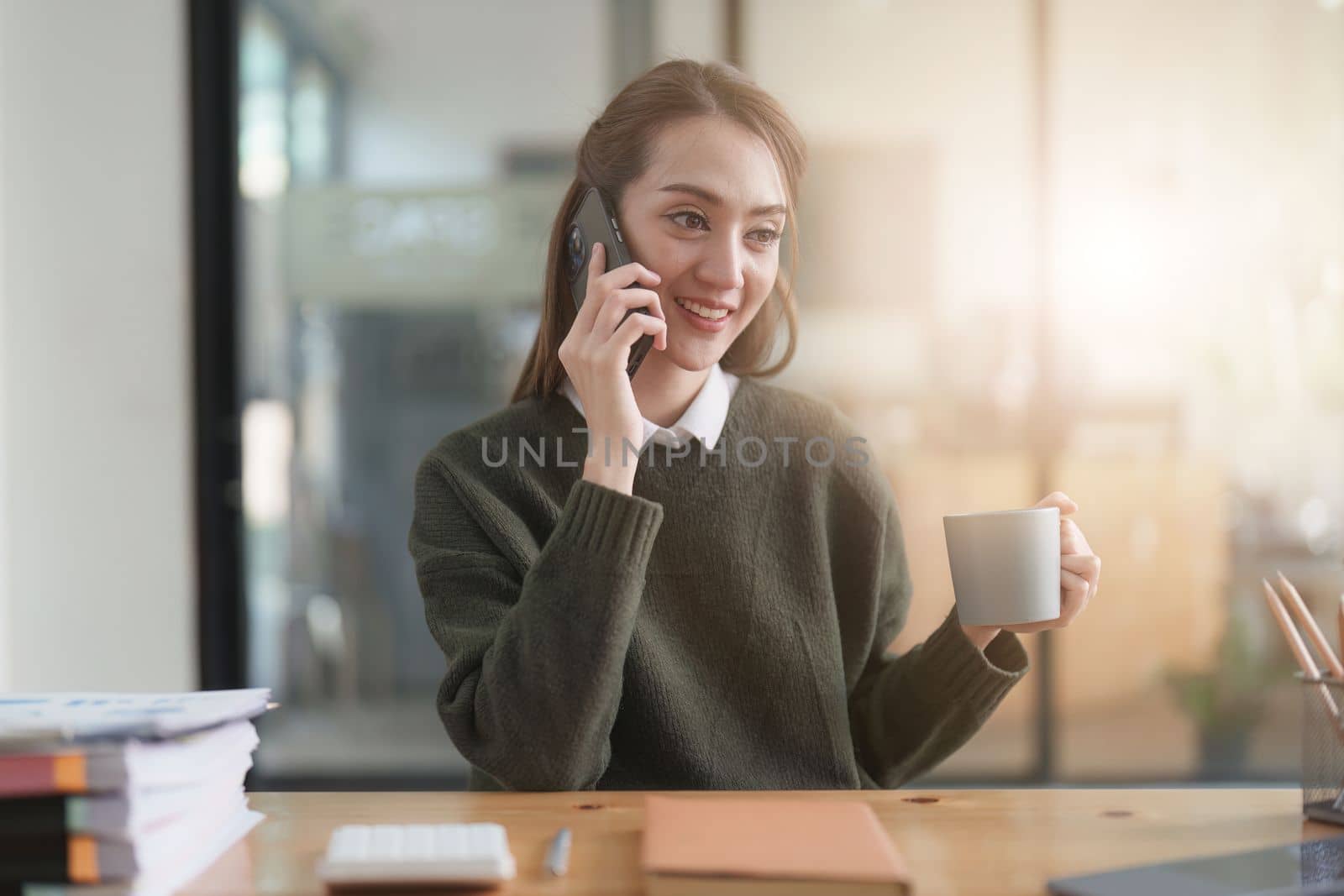 Beautiful Asian Business Woman talking on the mobile phone at her working place in office. Woman talking phone with client. Business Finance and accounting concept.