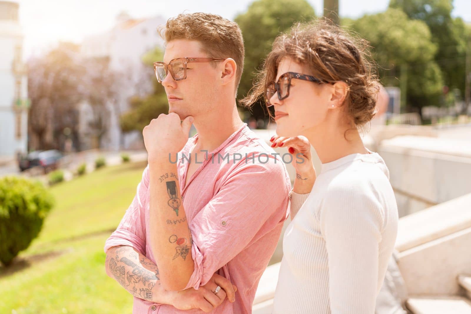 Young beautiful hipster couple in sunglasses in love walking on old city street by andreonegin