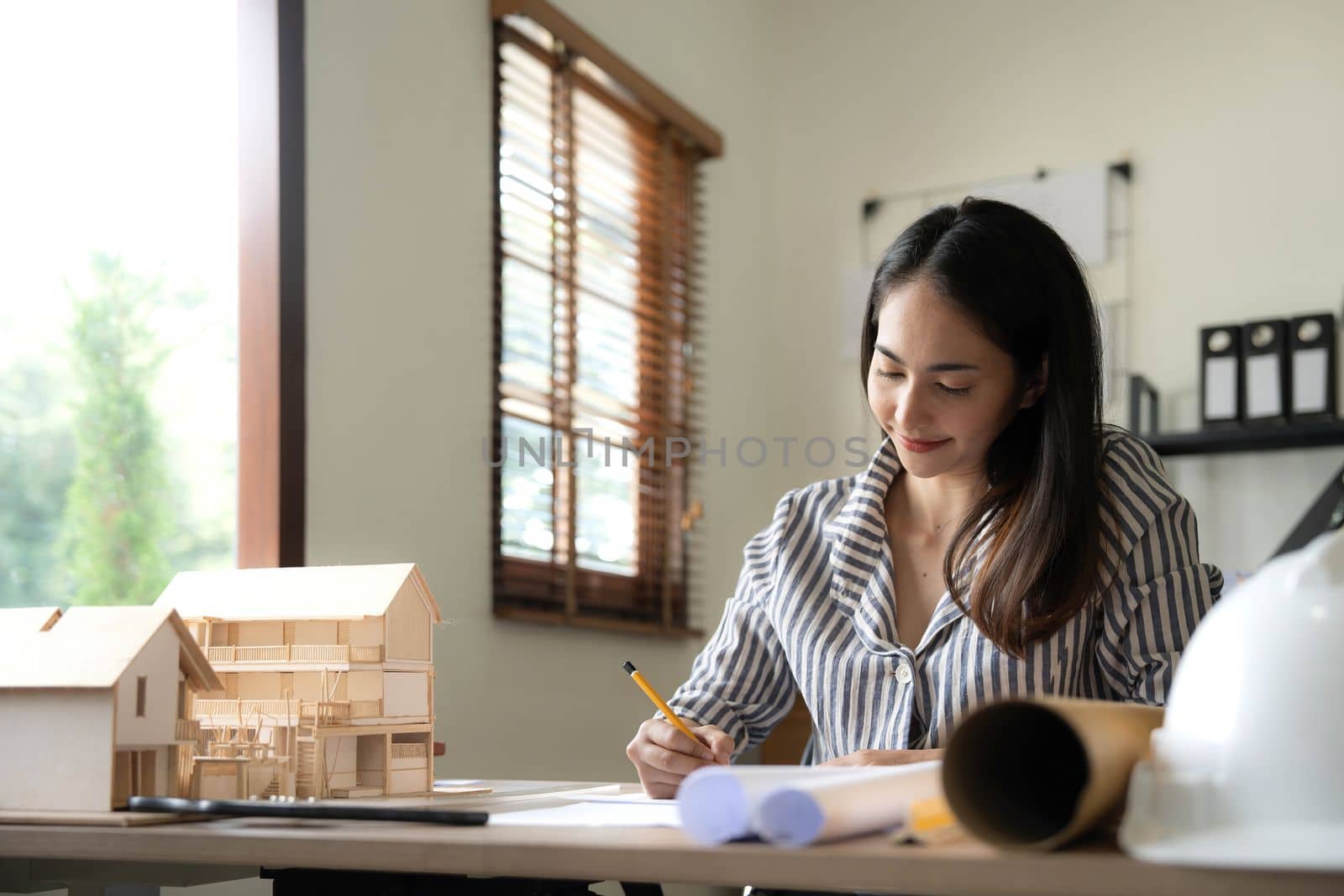 Architecture, building, construction and real estate concept - Happy smiling female architect with blueprint, ruler and living house model on table working at home office. Architect woman