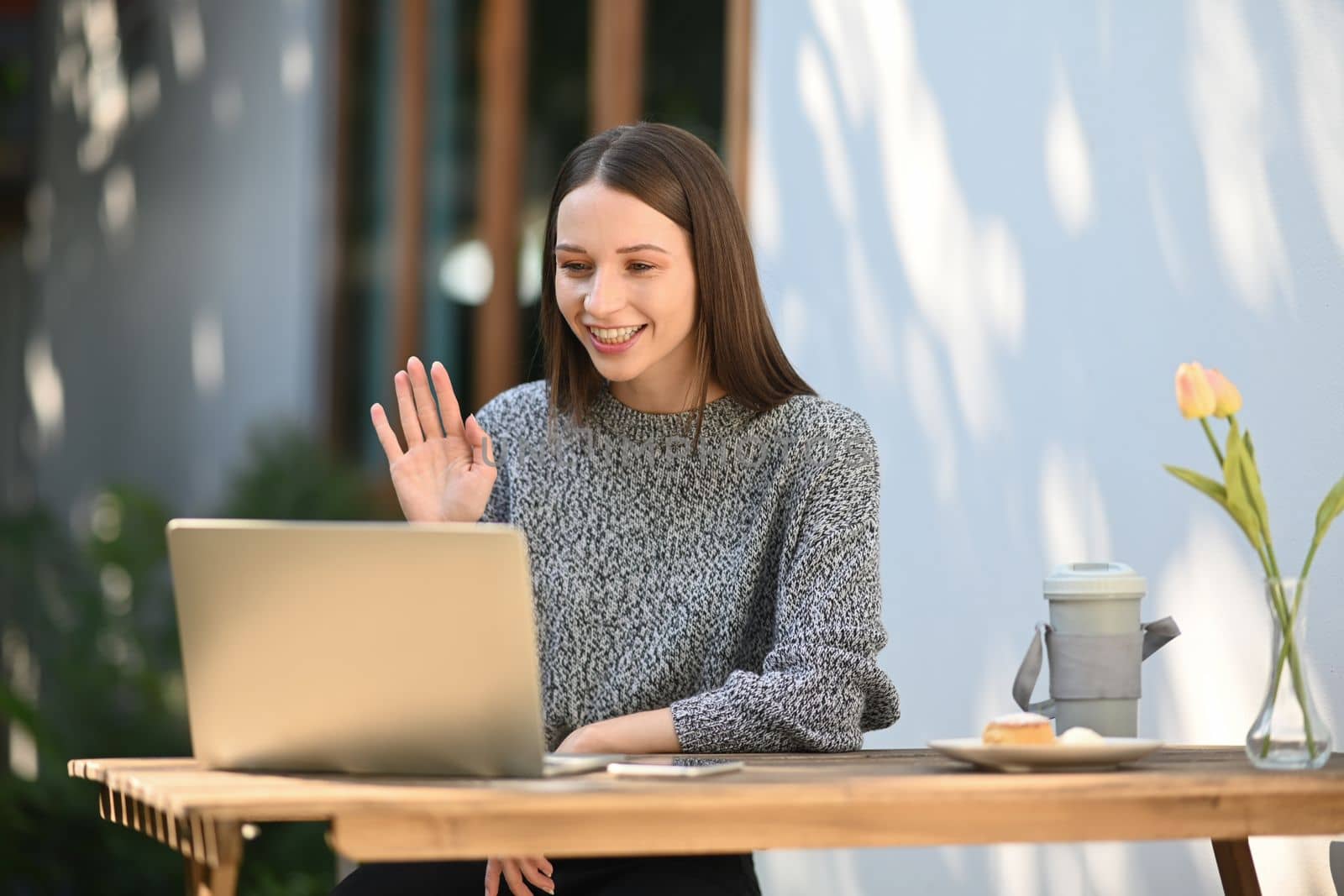 Beautiful young caucasian woman waving hand, having video call on laptop computer.