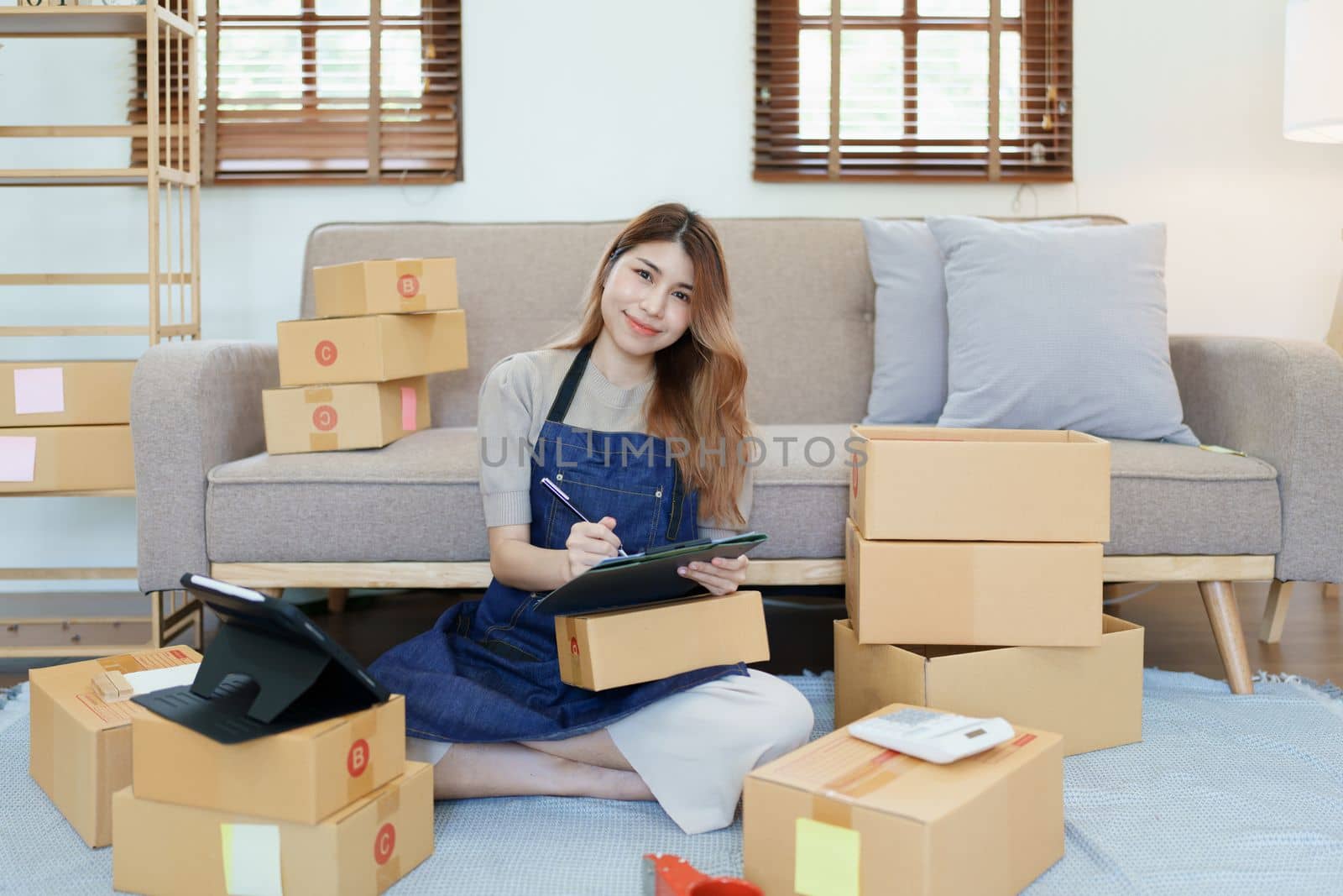 Starting small business entrepreneur of independent young Asian woman online seller is using smart phone and taking orders to pack products for delivery to customers. SME delivery concept by Manastrong