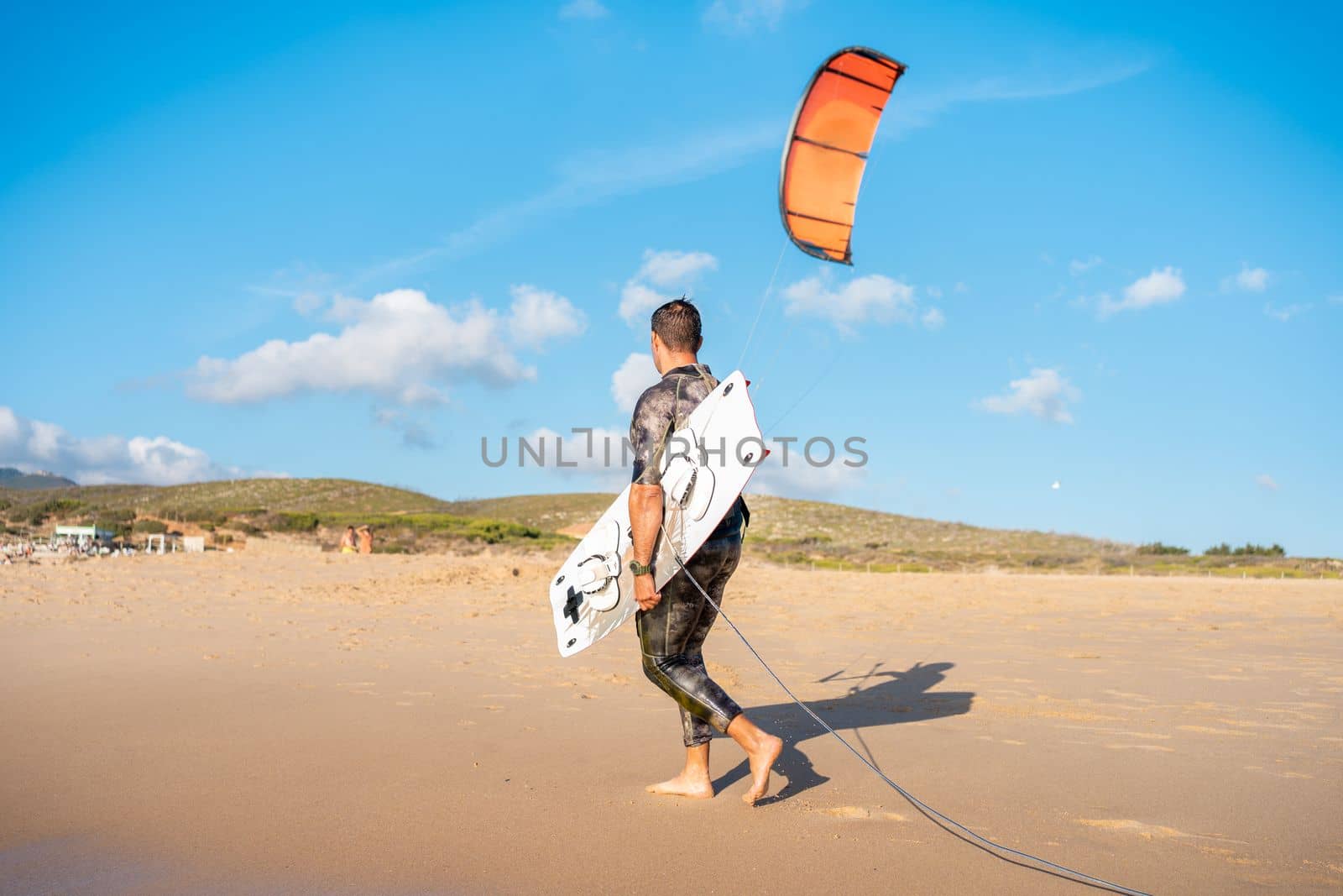 Portrait wave kitesurfer walking upwind at beach with his board and kite. Man kite surfer walk sand ocean beach with his kite surf board.