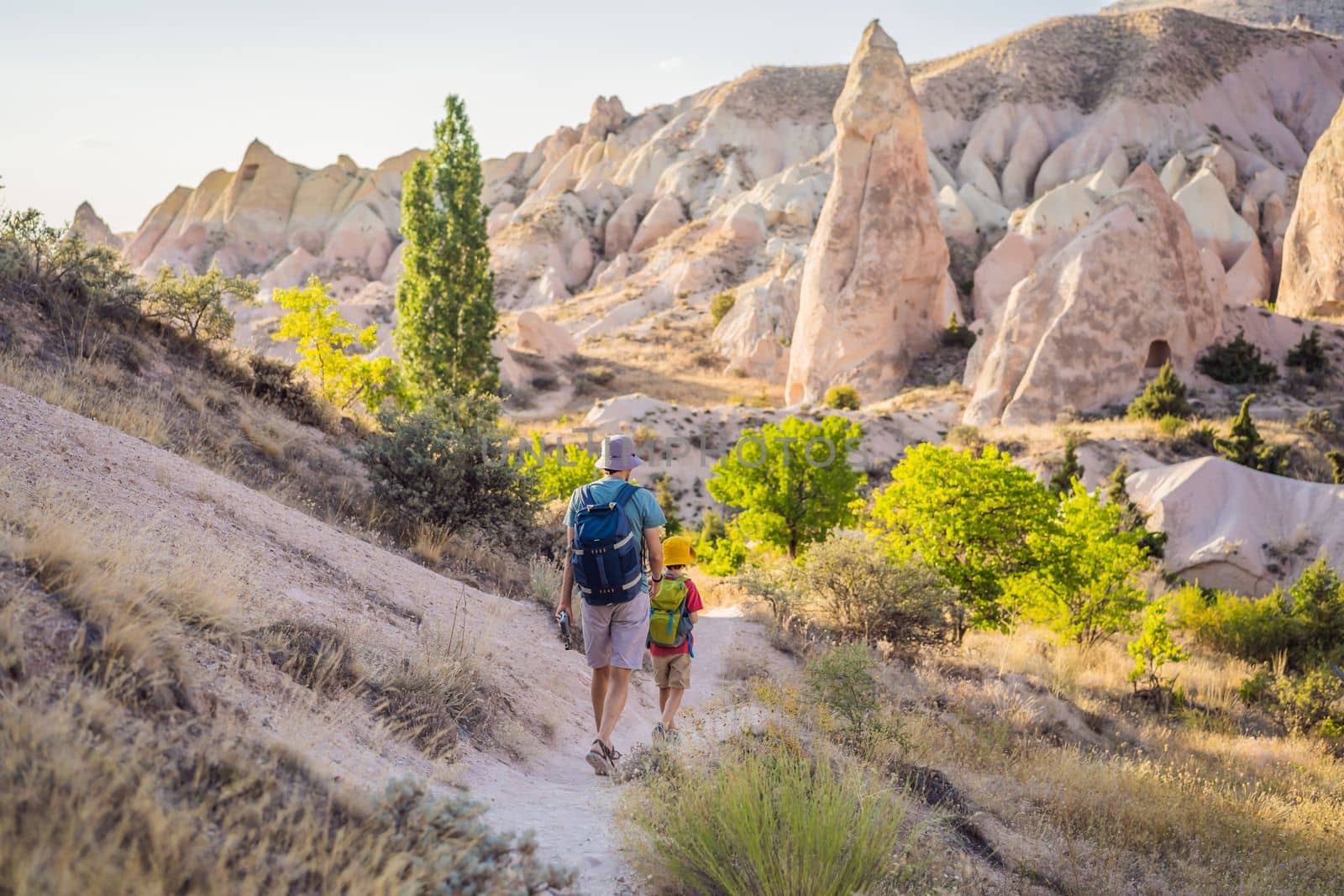 Father and son tourists exploring valley with rock formations and fairy caves near Goreme in Cappadocia Turkey.