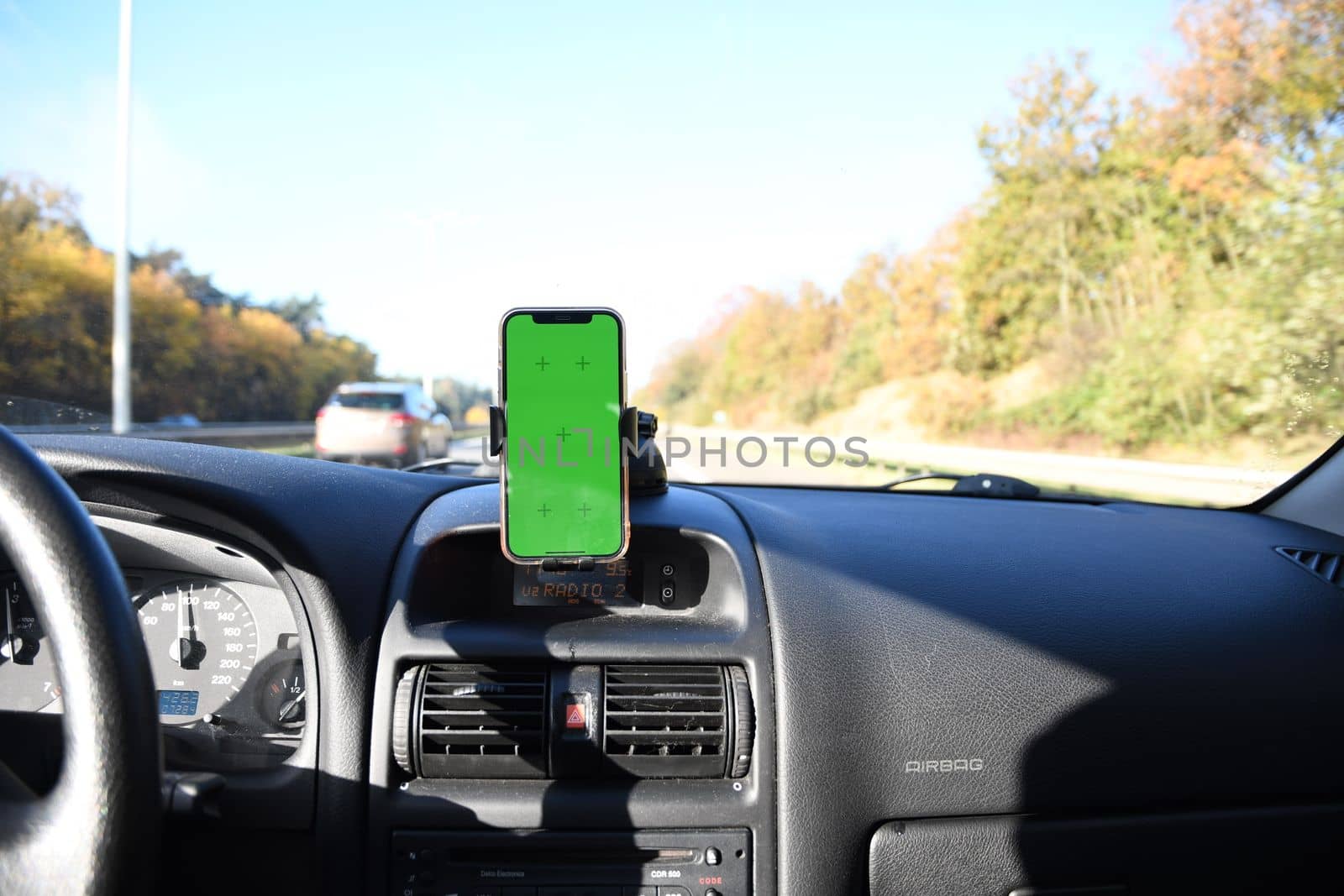Smartphone with green screen in windshield holder in car interior, road navigation and maps. High quality photo