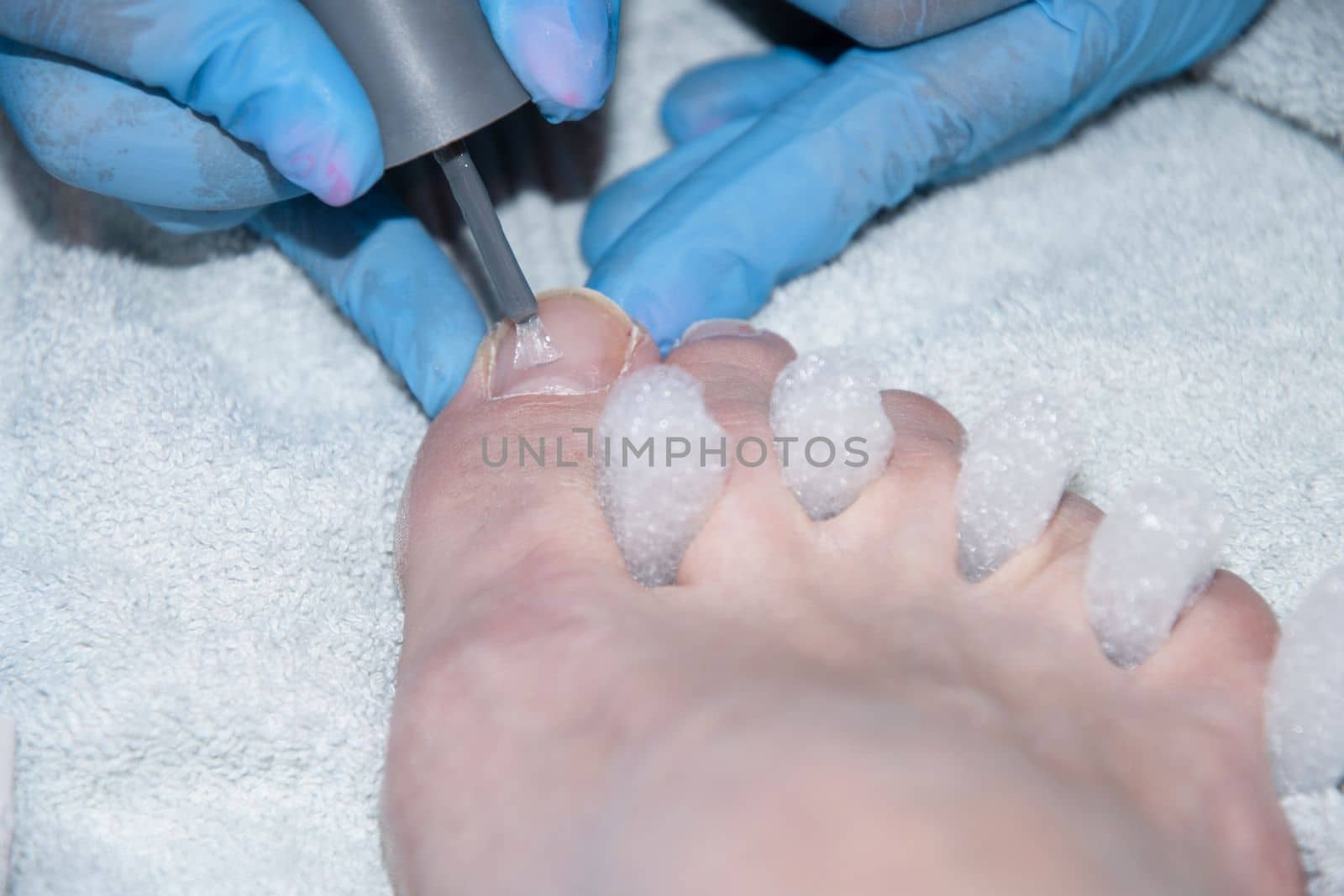  pedicure master applies gel polish on client's toe nails, Client's foot with white spongy toe separator,foot care at beauty center, High quality photo