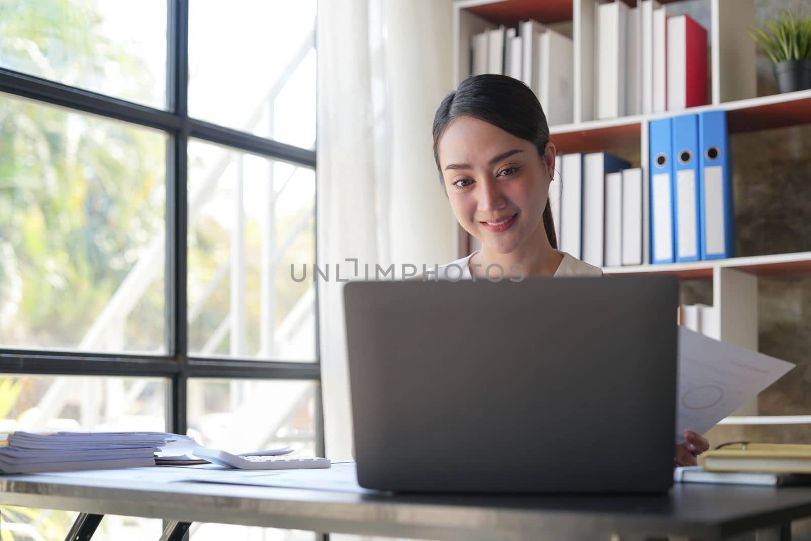 Asian Businesswoman Using laptop computer and working at office with calculator document on desk, doing planning analyzing the financial report, business plan investment, finance analysis concept...