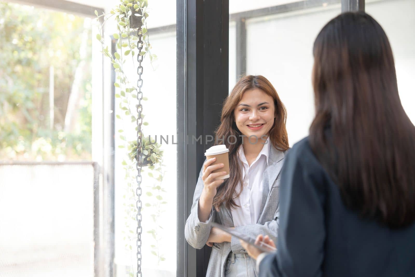 Happy two young Asian business woman holding coffee cup in coworking office by wichayada