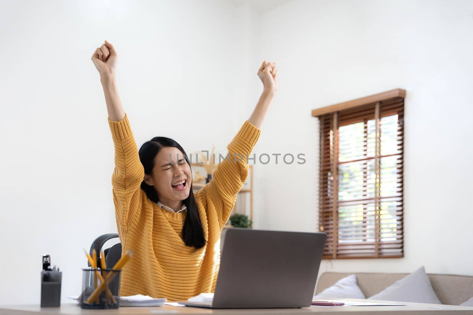 Excited happy woman looking at the laptop computer screen, celebrating an online win, overjoyed young asian female screaming with joy at home.