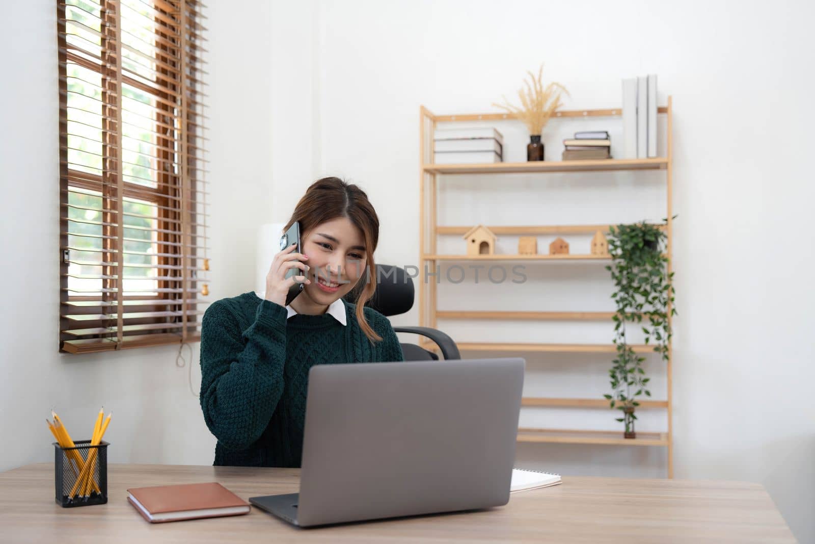 Beautiful Asian woman using laptop and smartphone with a happy face standing and smiling with a confident at home