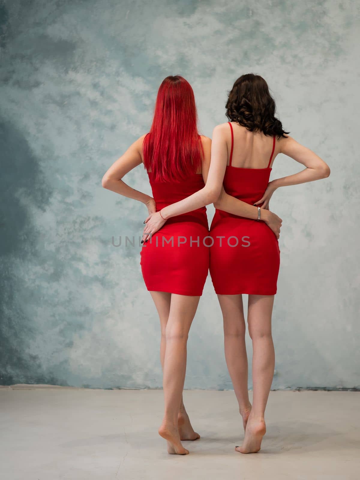 Full-length portrait of two tenderly embracing women dressed in identical red dresses. Lesbian intimacy