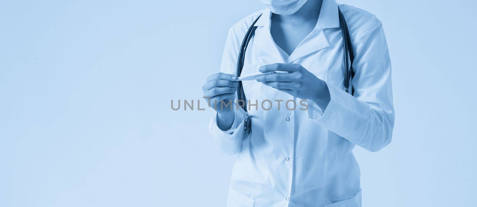 Doctor wearing face mask looking at measurement on medical thermometer over white background with copy space by Mariakray