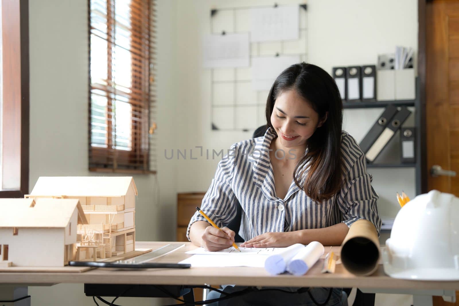 Architecture, building, construction and real estate concept - Happy smiling female architect with blueprint, ruler and living house model on table working at home office. Architect woman