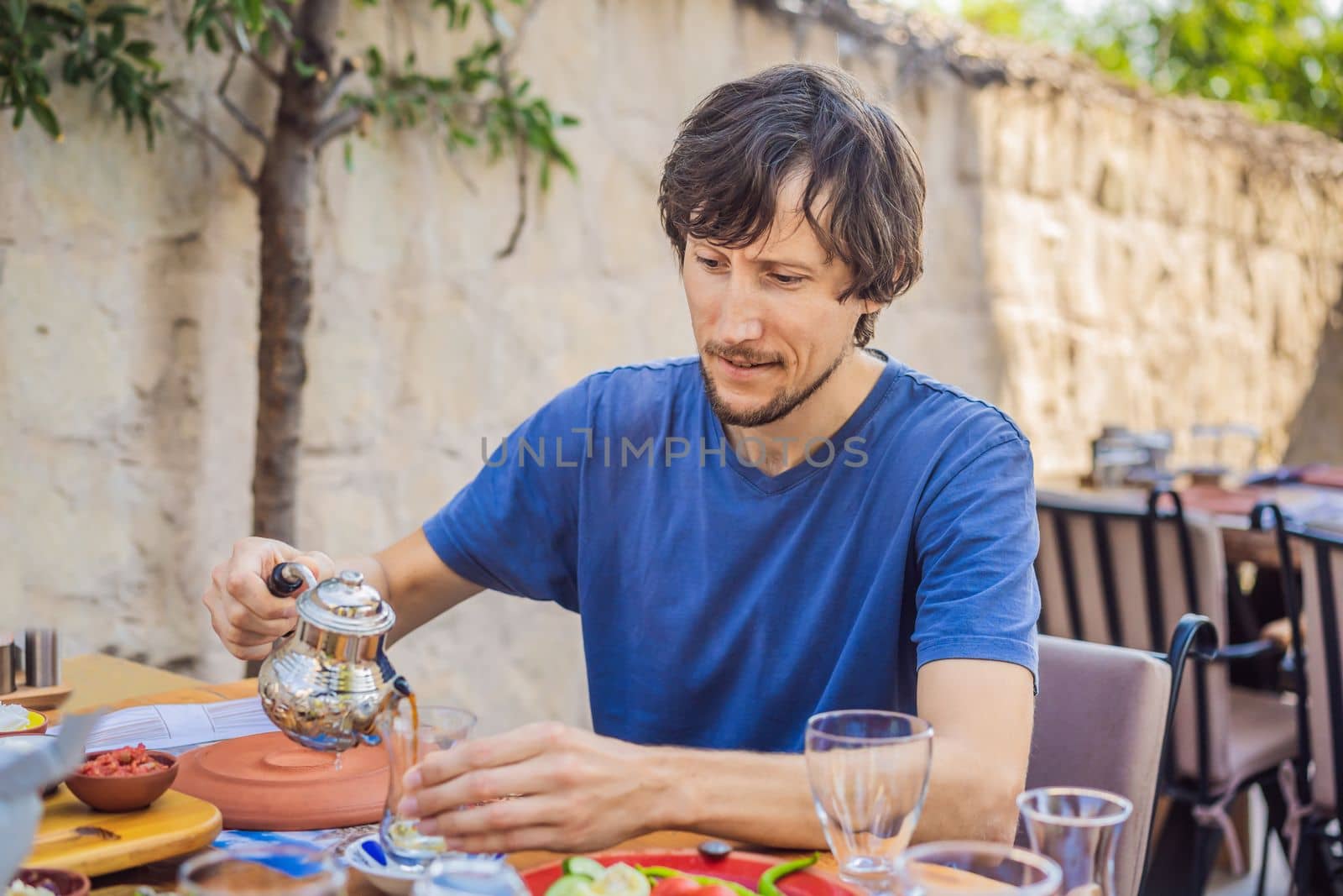 Man eating turkish breakfast. Turkish breakfast table. Pastries. Vegetables. Olives. Cheeses, fried eggs. Jams, tea in copper pot and tulip glasses. Wide composition.