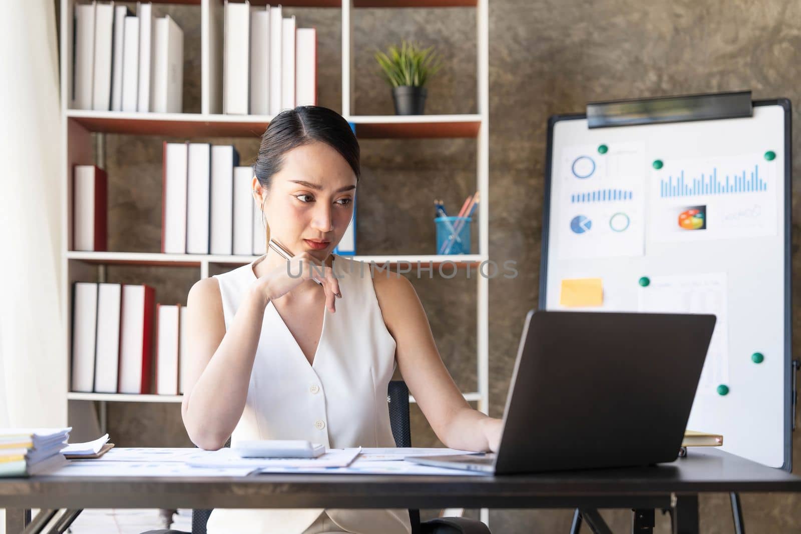 Asian Businesswoman Using laptop computer and working at office with calculator document on desk, doing planning analyzing the financial report, business plan investment, finance analysis concept...