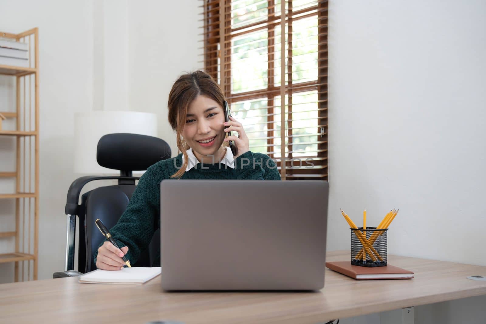 Beautiful Asian woman using laptop and smartphone with a happy face standing and smiling with a confident at home