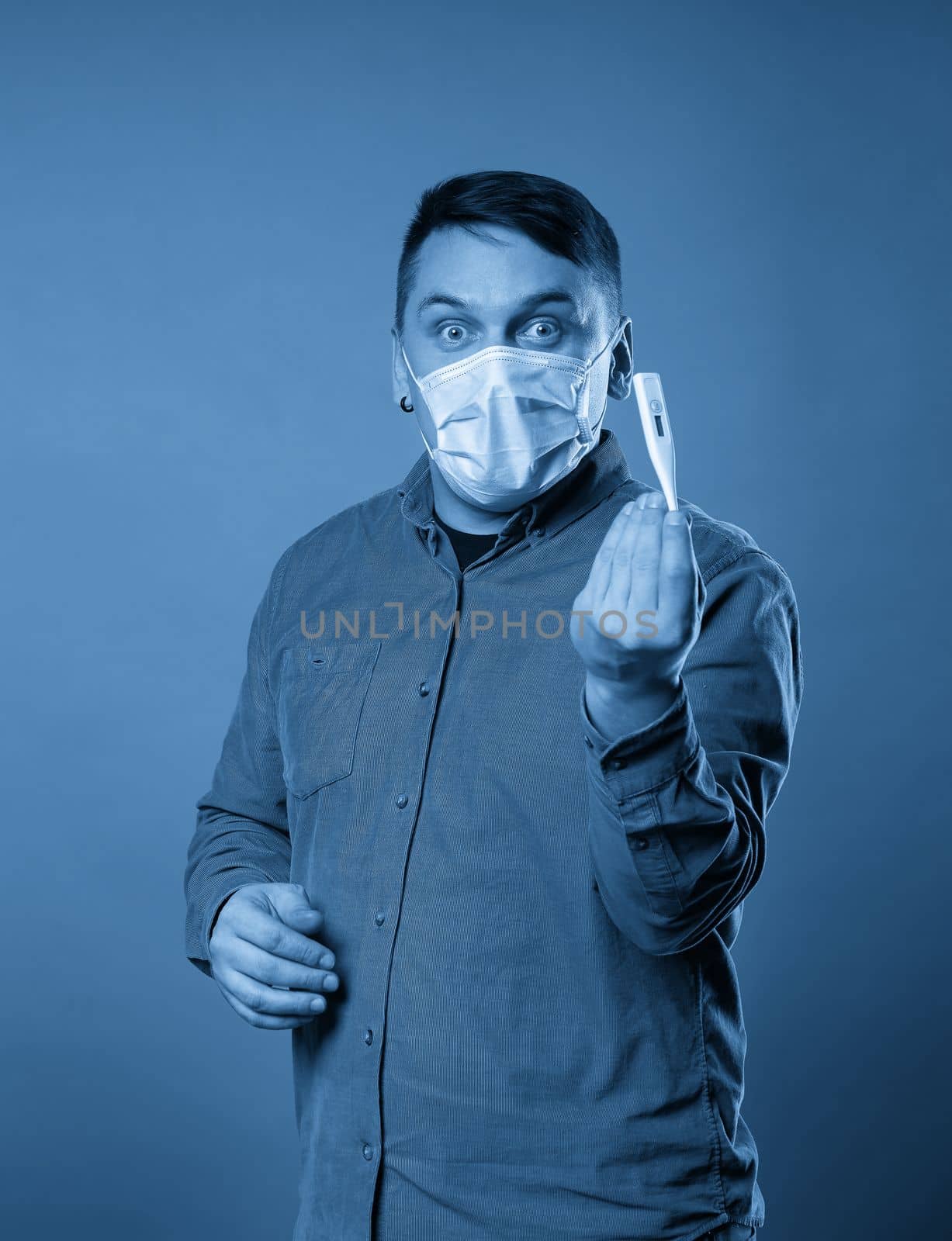 Young man in casual cloth wearing medical protective mask excited, stressed and frightened after read very high temperature result from digital thermometer, illness concept by Mariakray