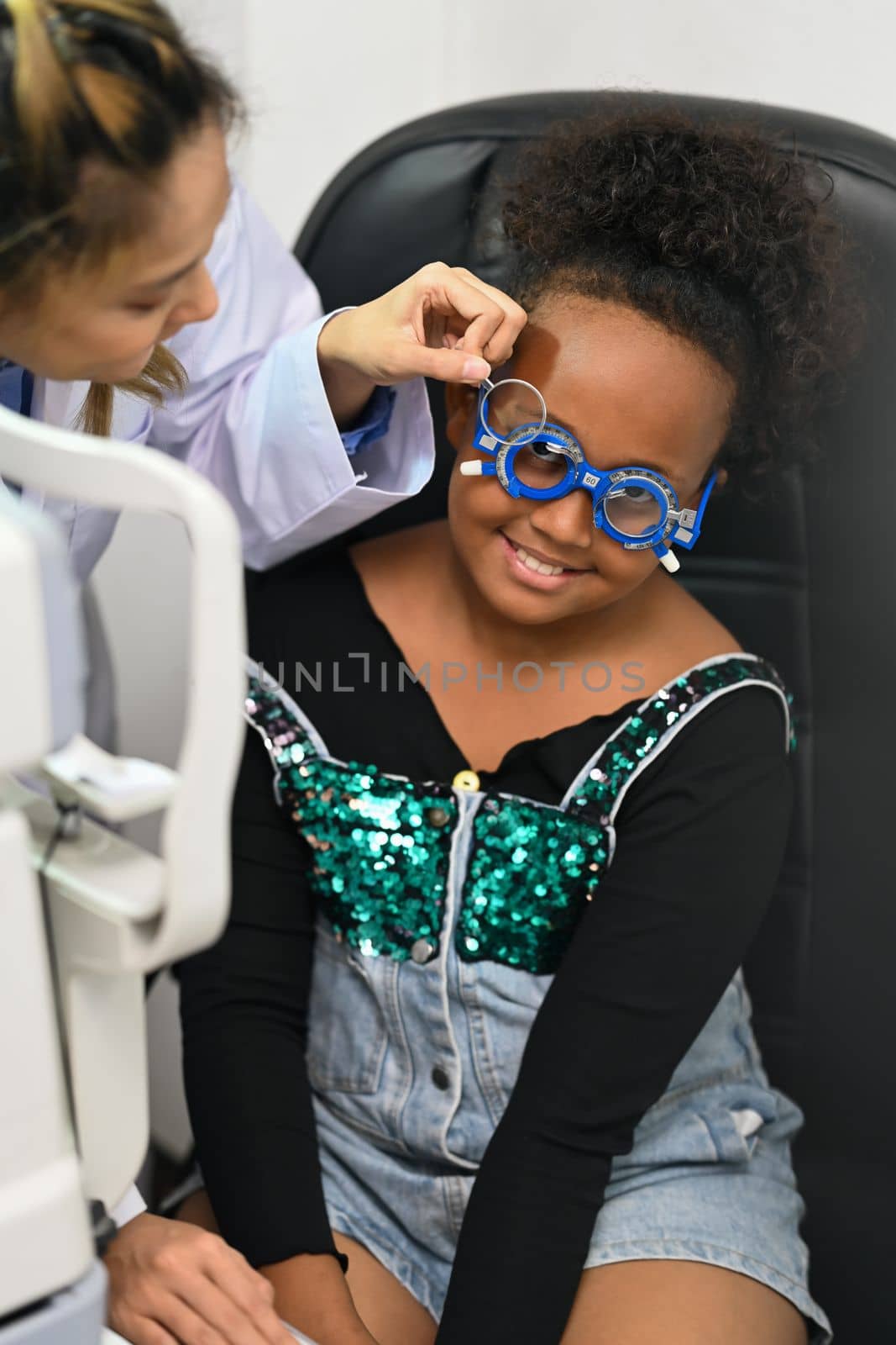 Smiling girl checking eye vision with ophthalmologist for spectacles glasses. Eye health check, ophthalmology concept.