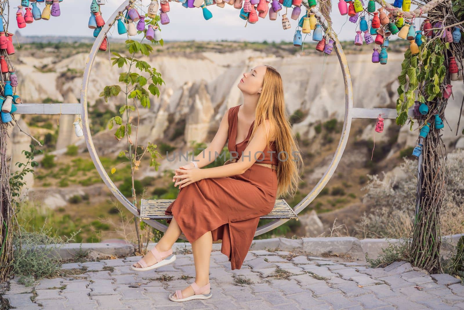 Young woman exploring valley with rock formations and fairy caves near Goreme in Cappadocia Turkey. Wish tree. Small multi-colored jugs with inscriptions, wishes hanging on the branches of a tree., against the backdrop of sand ruins and blue sky.