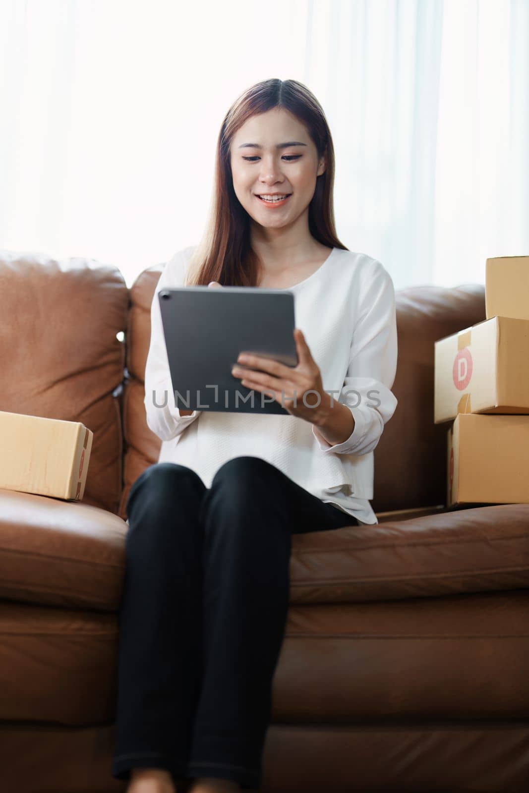 Starting small business entrepreneur of independent young Asian woman online seller is using tablet computer and taking orders to pack products for delivery to customers. SME delivery concept by Manastrong