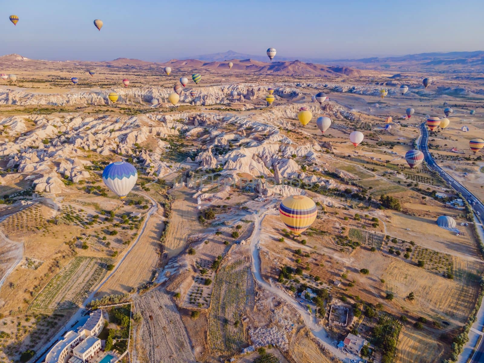 Colorful hot air balloons flying over at fairy chimneys valley in Nevsehir, Goreme, Cappadocia Turkey. Spectacular panoramic drone view of the underground city and ballooning tourism. High quality.