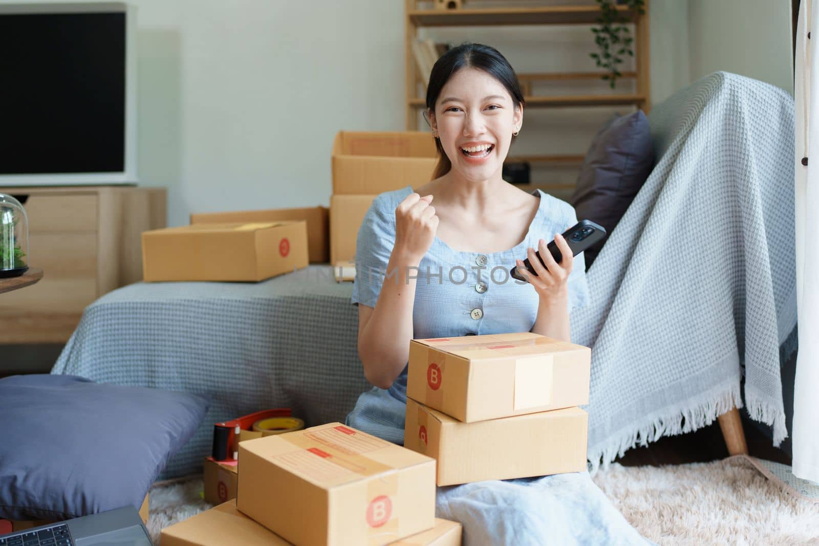 Starting small business entrepreneur of independent Asian woman smiling using computer laptop with cheerful success of online marketing package box items and SME delivery concept by Manastrong