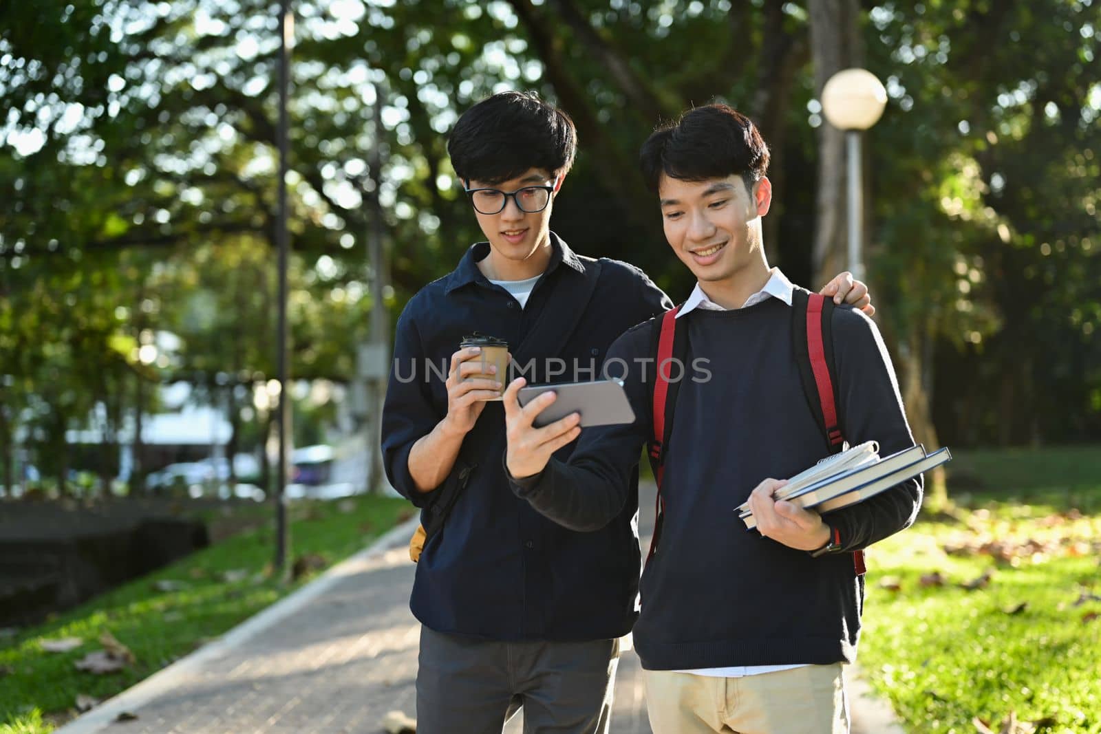 Two asian students talking to each other after classes while walking in university campus outdoors.