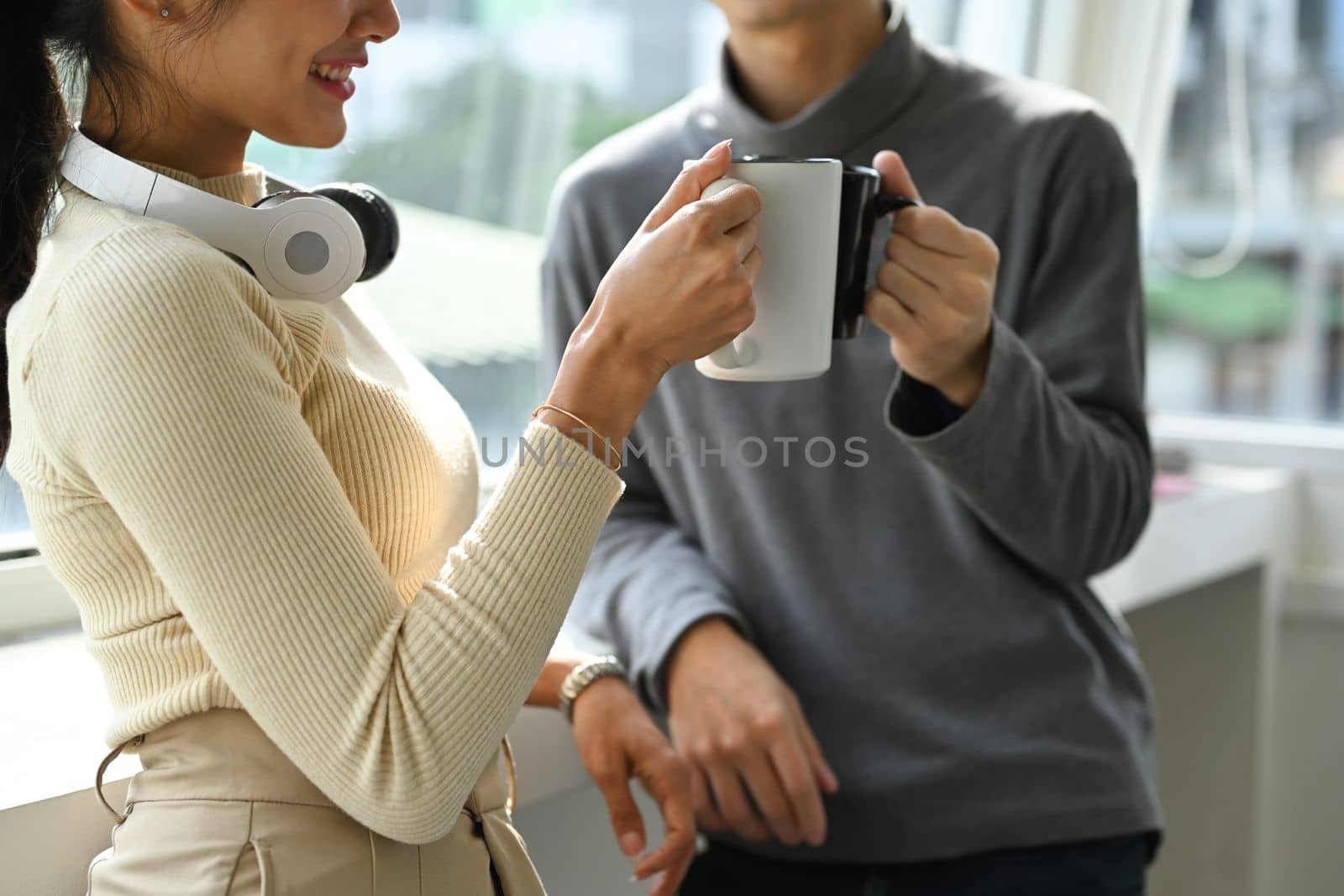 Cropped shot of tea young employee having conversation during break while standing in near office window by prathanchorruangsak