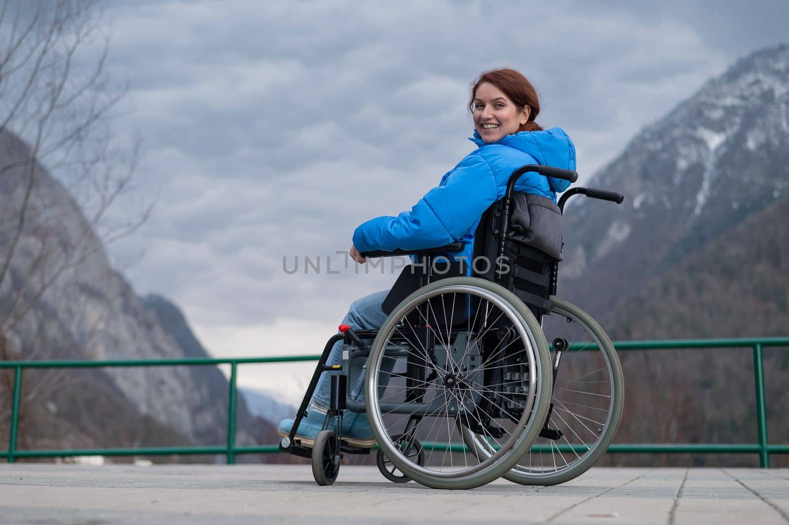 A woman in a wheelchair on a point view admires the high mountains. Thrust to life