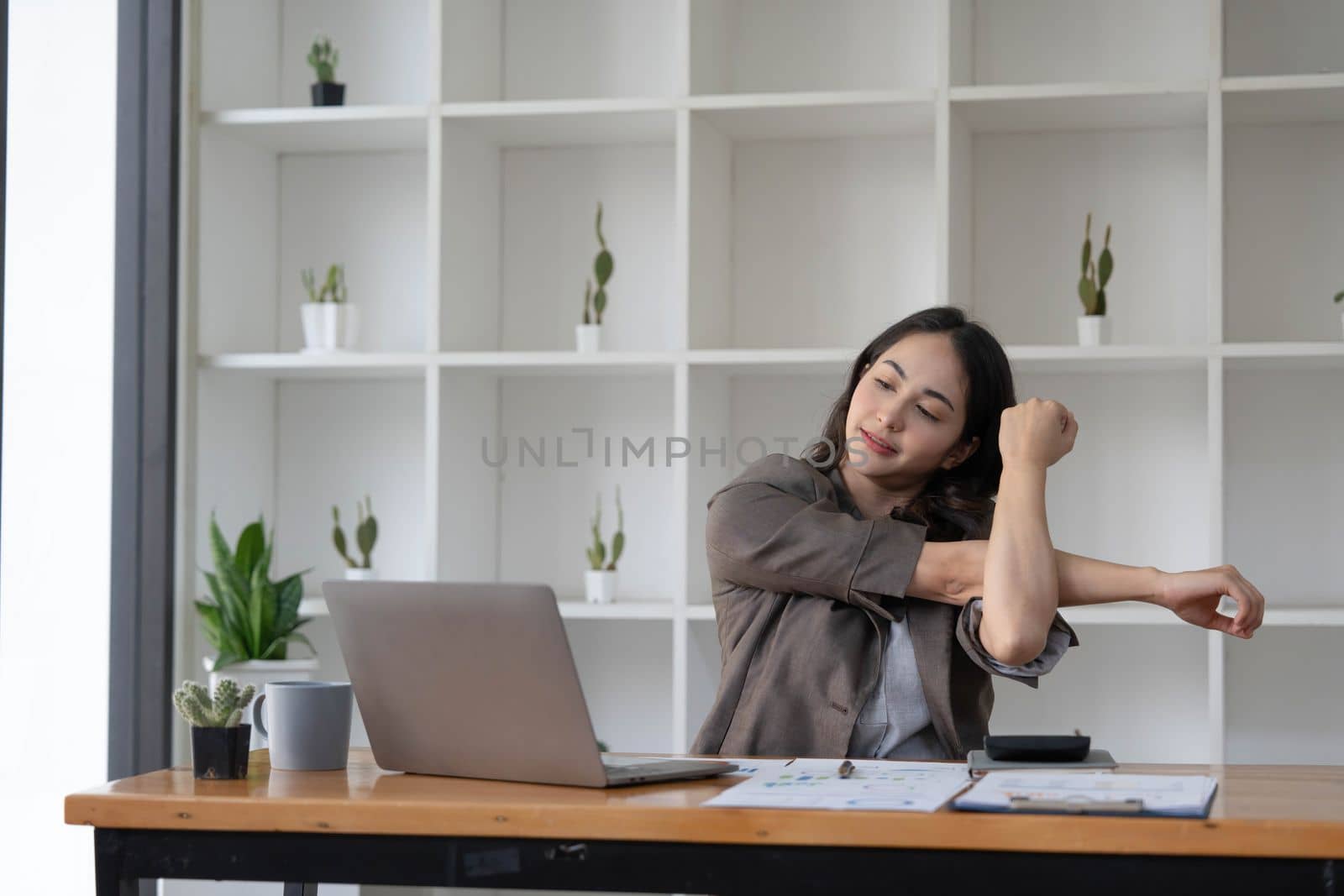 Asian businesswoman stretches her arms to relax her tired muscles from working at her desk all day at the office...