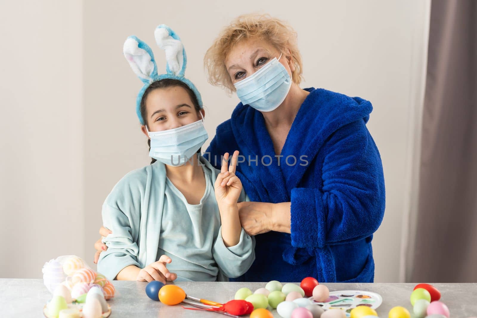 grandmother and children are painting eggs. Happy family are preparing for Easter. Cute little girls wearing bunny ears