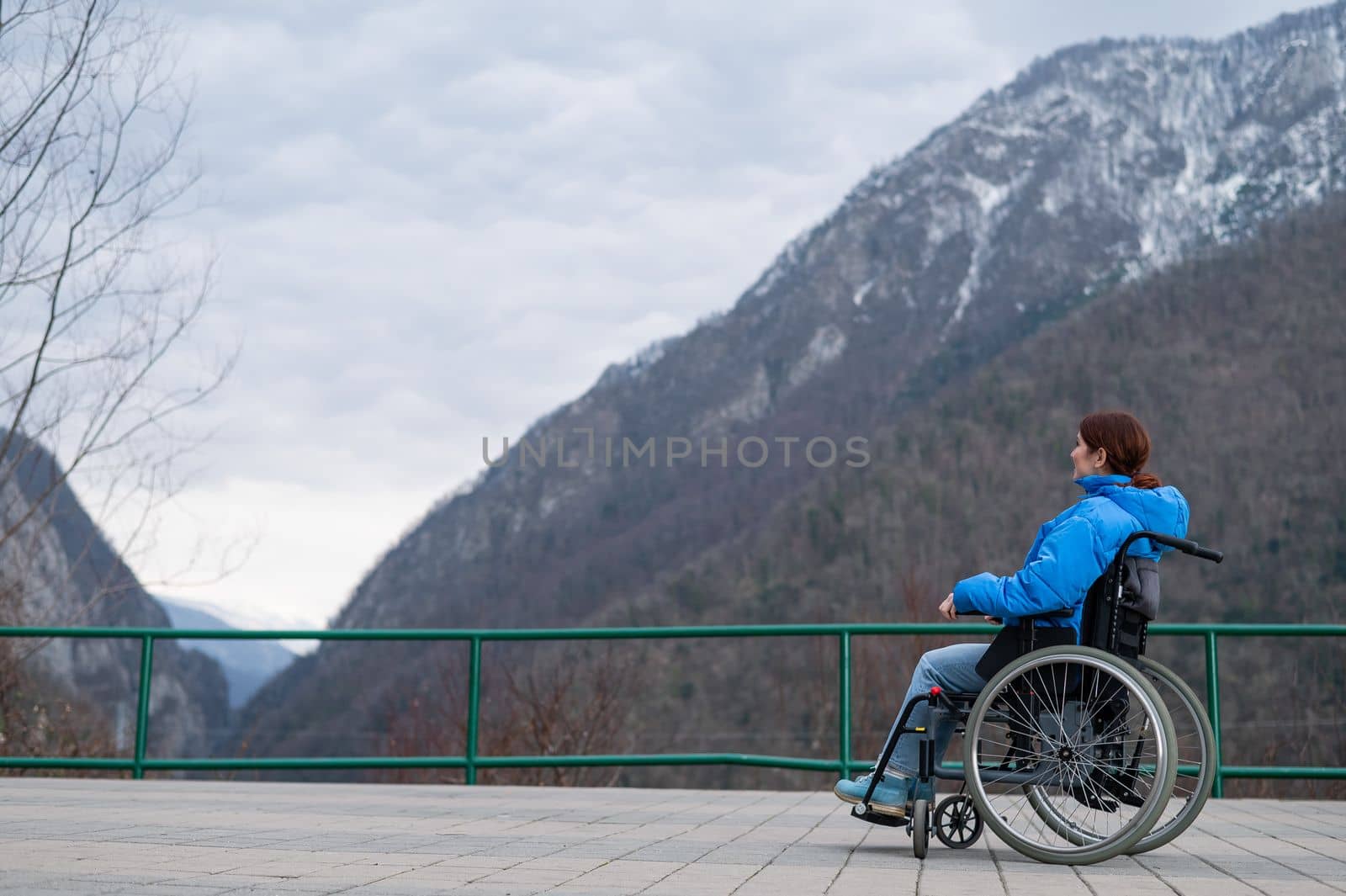 A woman in a wheelchair on a point view admires the high mountains. Thrust to life