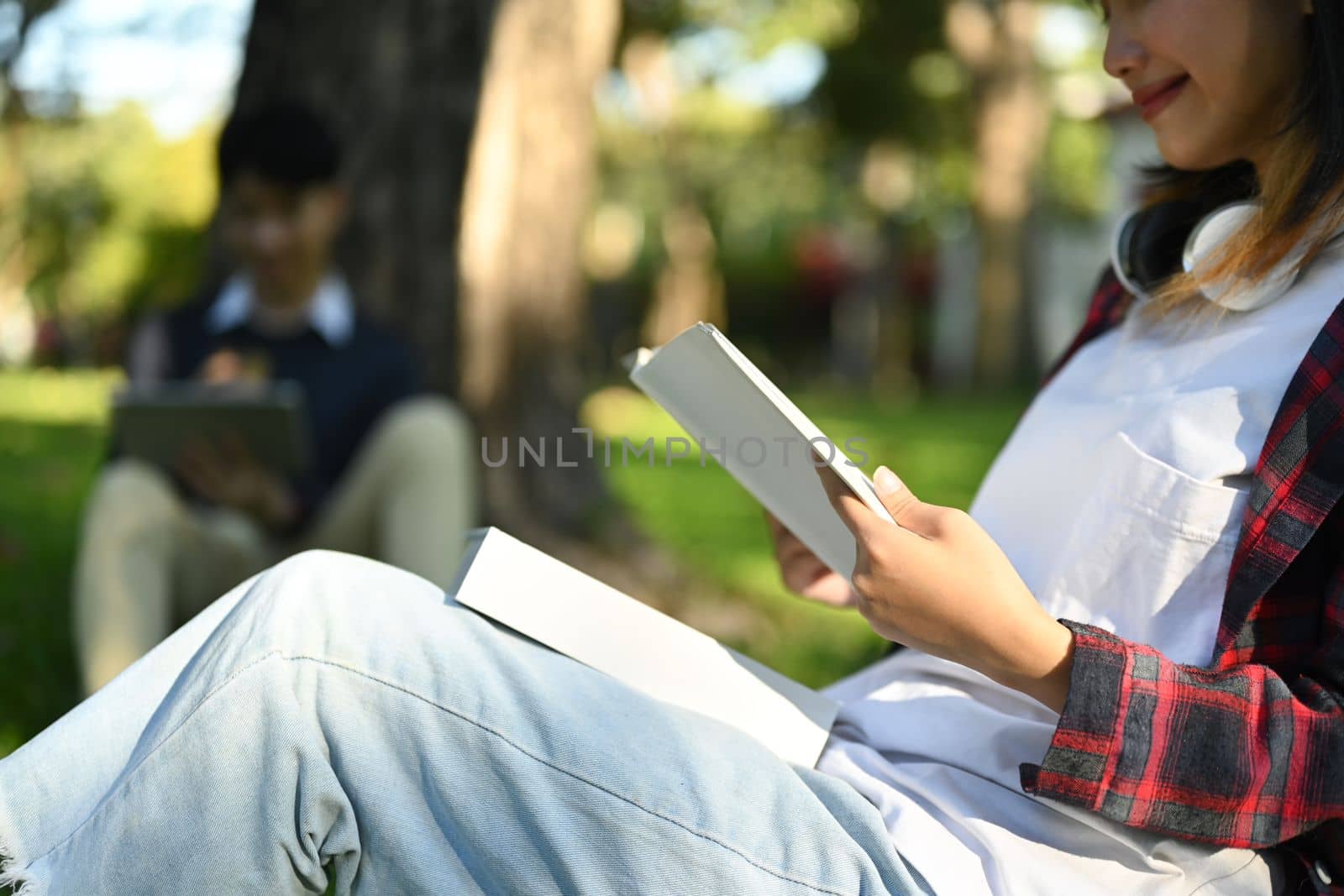 Cropped shot of smiling female student reading books at sunny beautiful garden background.