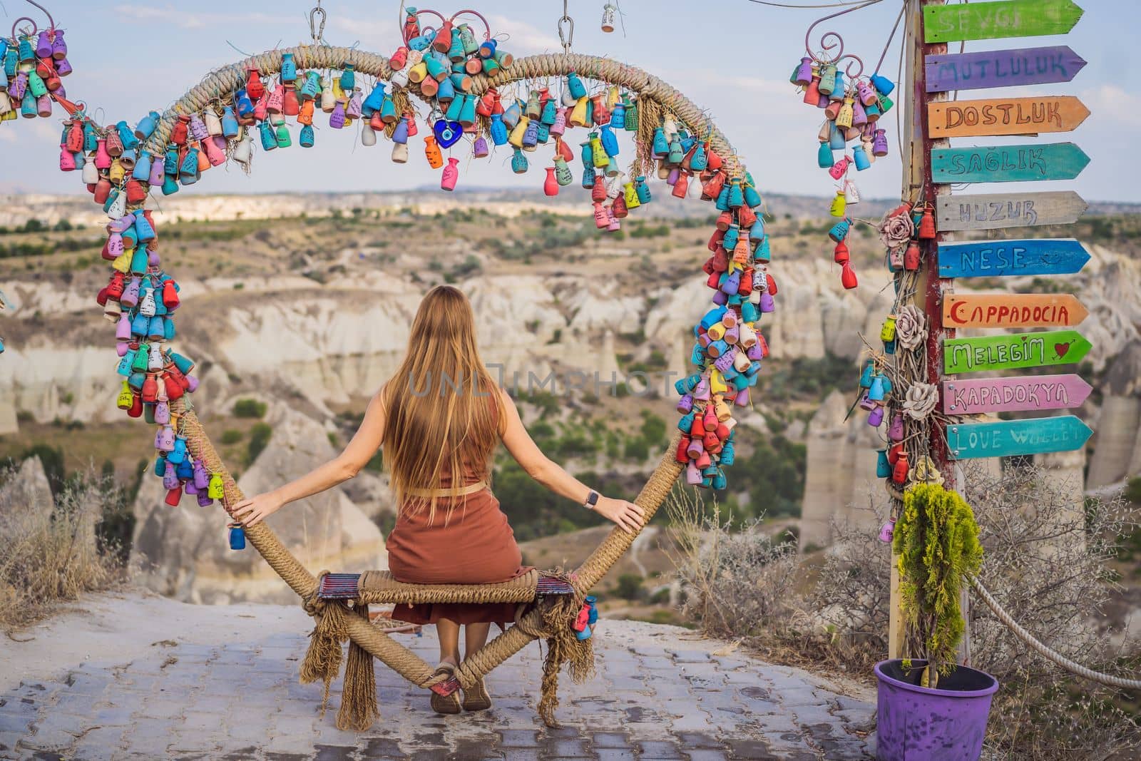Young woman exploring valley with rock formations and fairy caves near Goreme in Cappadocia Turkey. Wish tree. Small multi-colored jugs with inscriptions, wishes hanging on the branches of a tree., against the backdrop of sand ruins and blue sky.