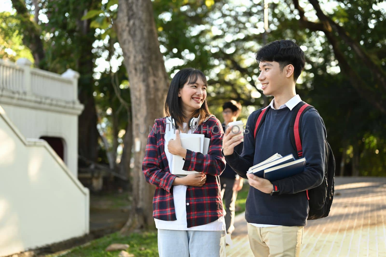 Two friendly university students are talking to each other after classes while walking in university campus outdoors.