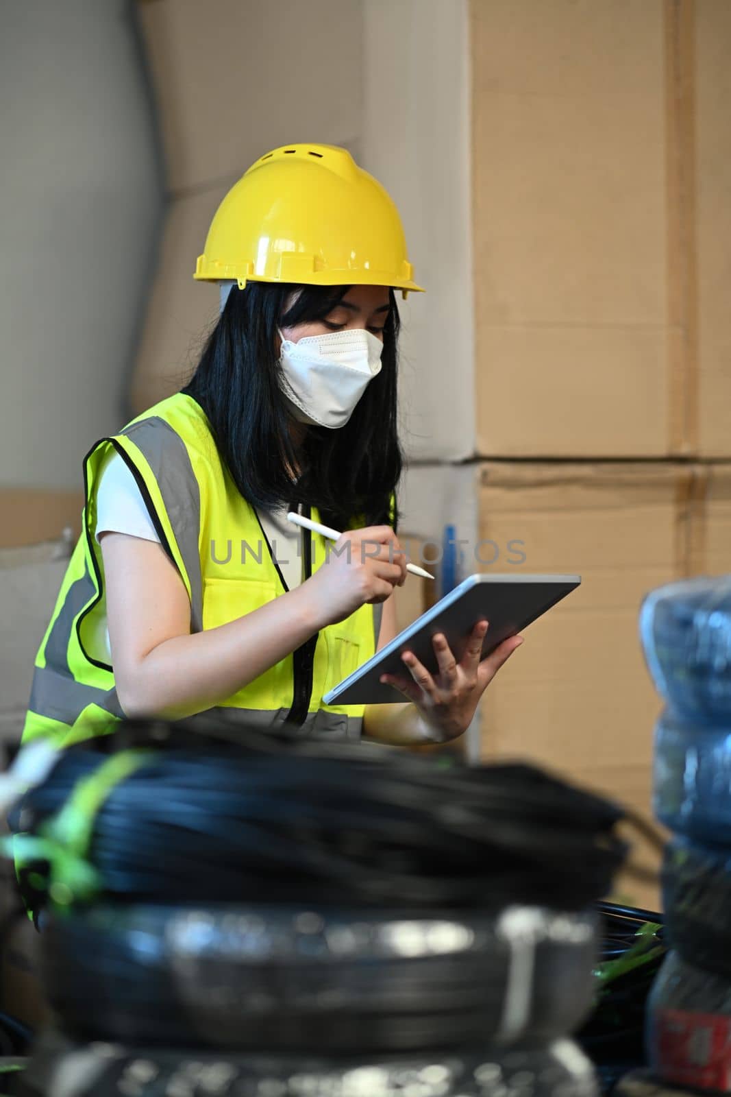 Image of female manager in yellow vest tracking supply order details on digital tablet. Logistic industry concept by prathanchorruangsak